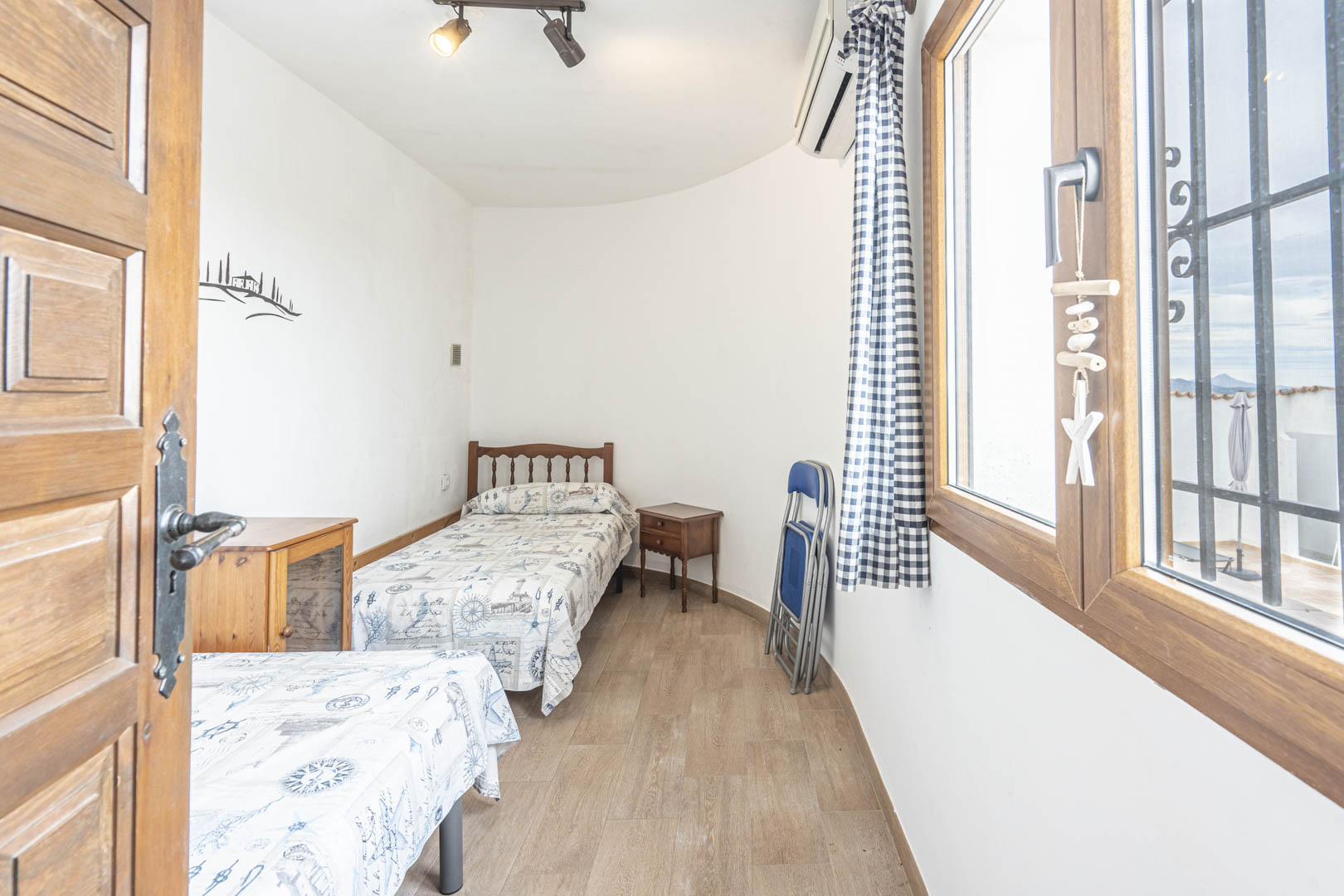Lichte slaapkamer met twee eenpersoonsbedden, nautisch decor en uitzicht naar buiten vanuit het houten raam.