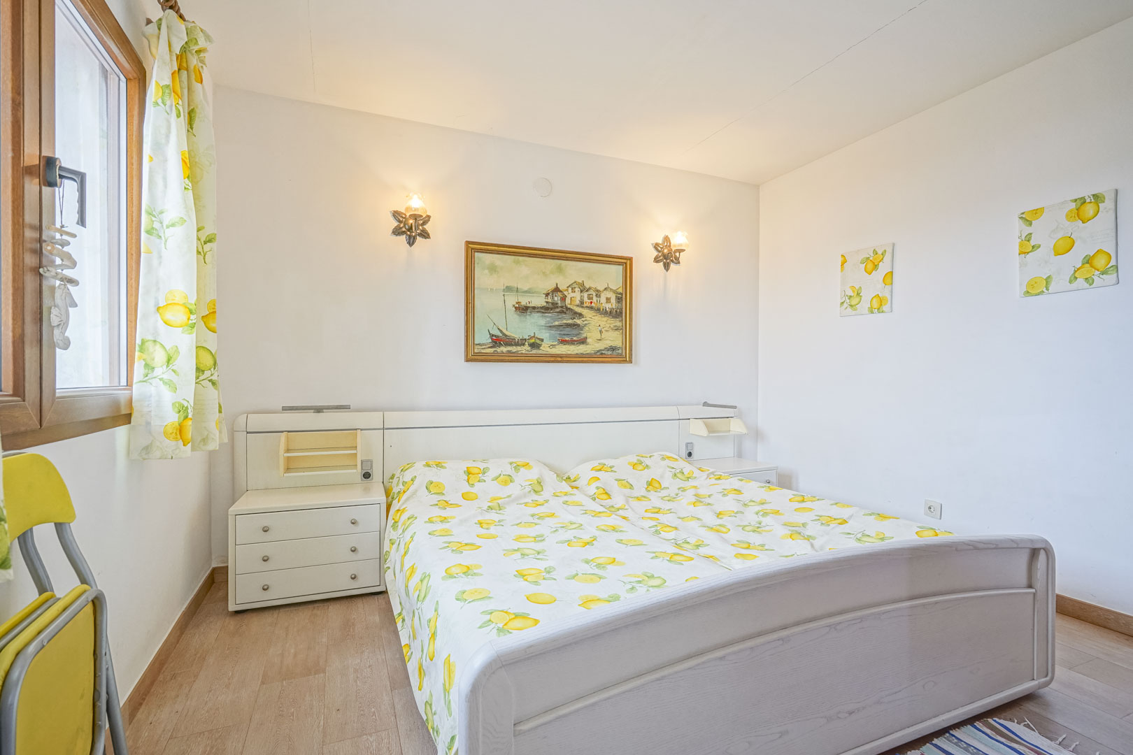Lichte slaapkamer met tweepersoonsbed, wit hoofdeinde met ingebouwde nachtkastjes en decoratie met citroenthema.