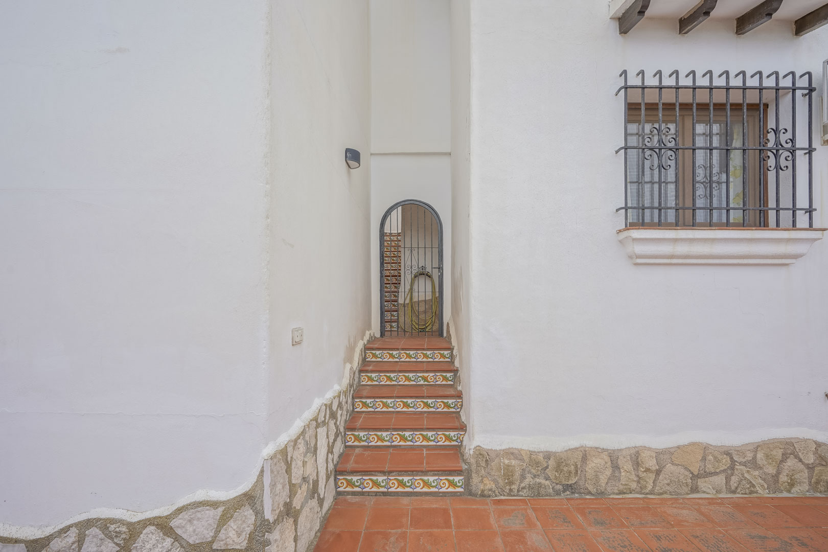 Villa-ingang met versierde keramische treden en smeedijzeren poort, rustieke details op de witte gevel.