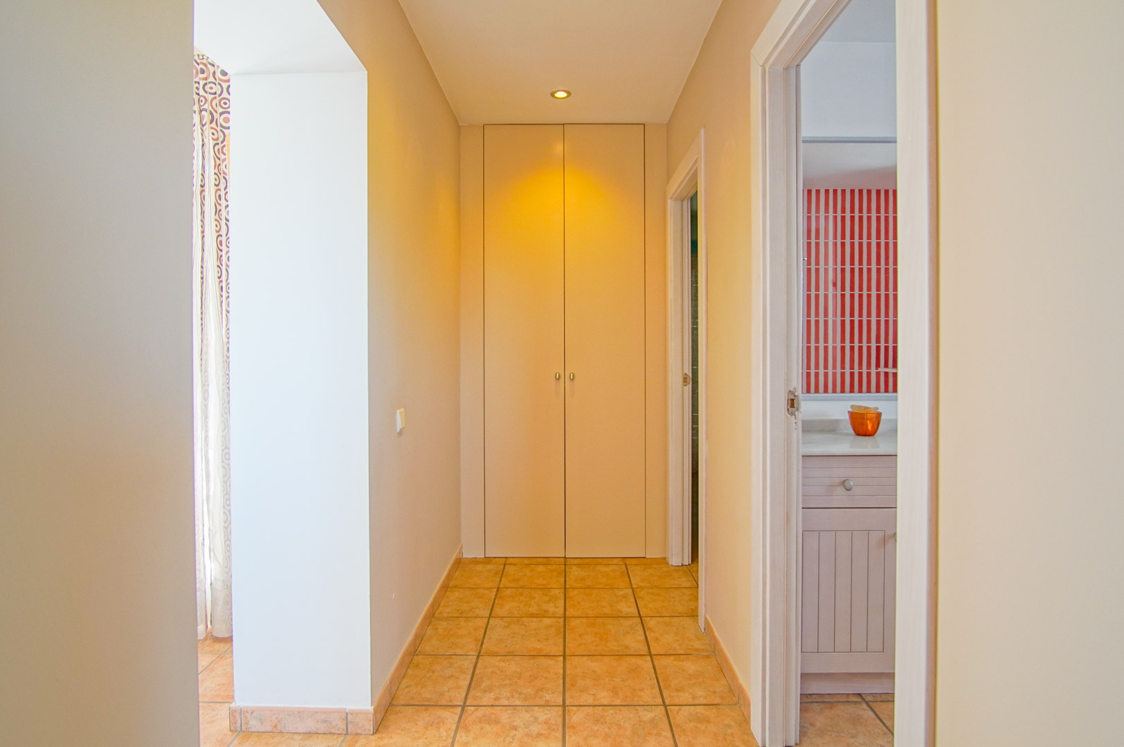 Hal met keramische vloertegels, voorzien van een kamerhoge inbouwkast en toegang tot een badkamer met opvallende rood-wit gestreepte wandtegels.