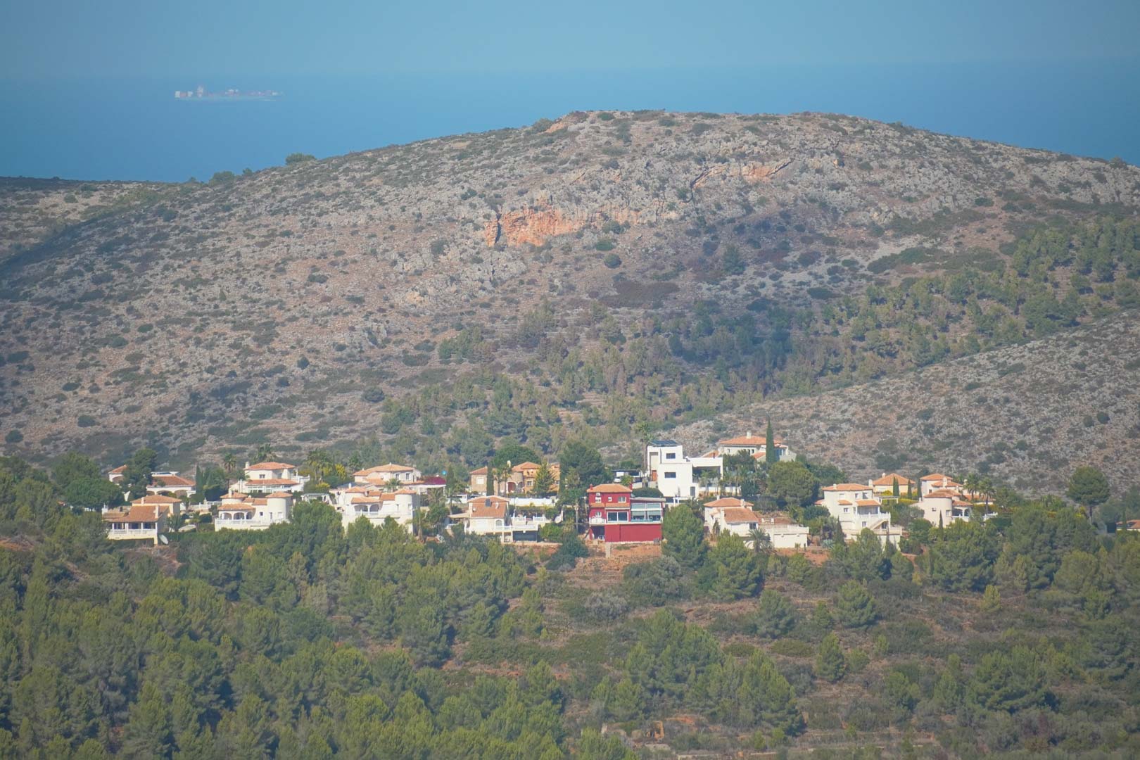 Panoramisch uitzicht vanaf de woning over de villawijk in de heuvels, omringd door pijnbomen, met de bergen en de Middellandse Zee aan de horizon.