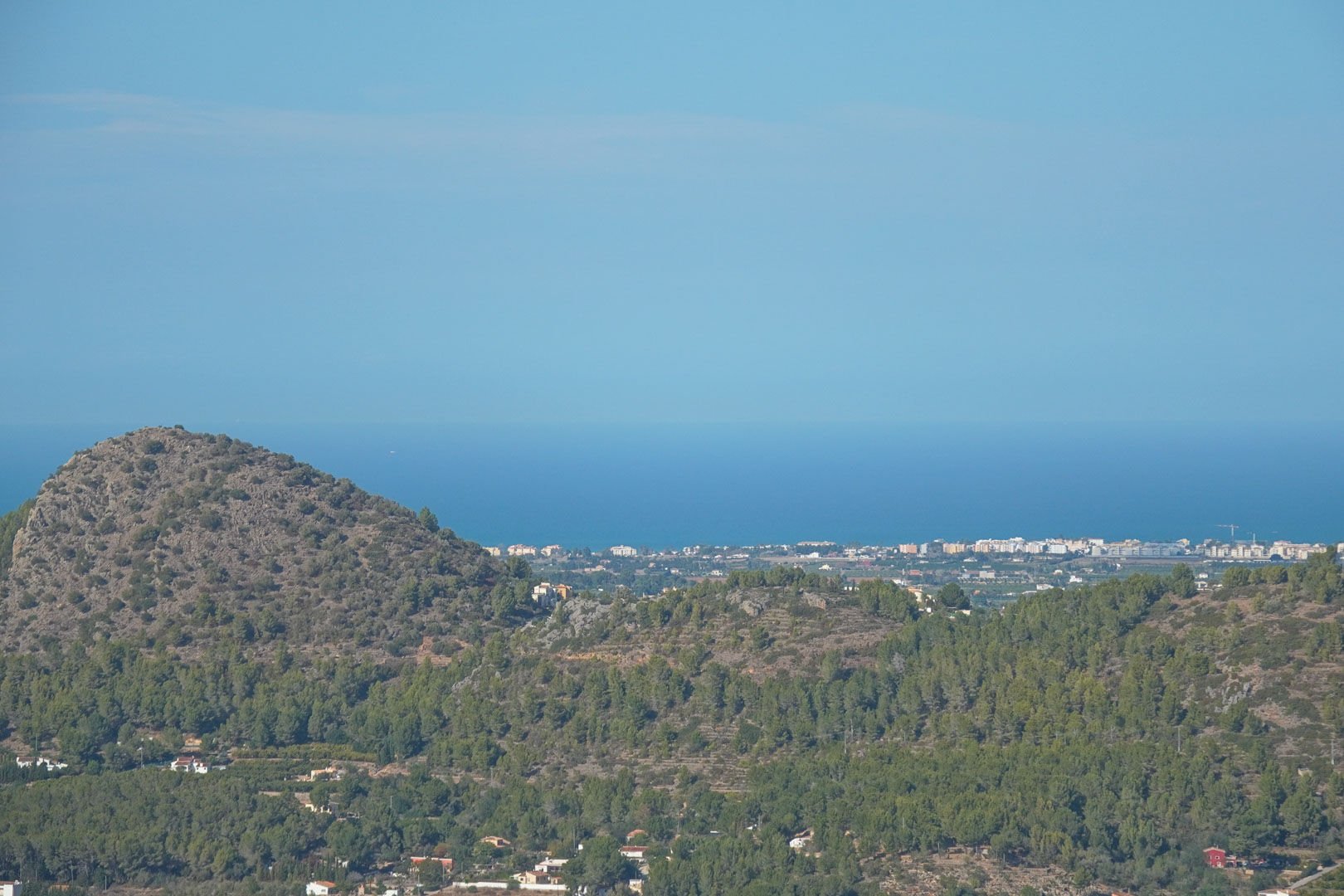 Panoramisch uitzicht vanaf het landgoed over de mediterrane bergen, verspreide kustbebouwing en de blauwe horizon van de Middellandse Zee.