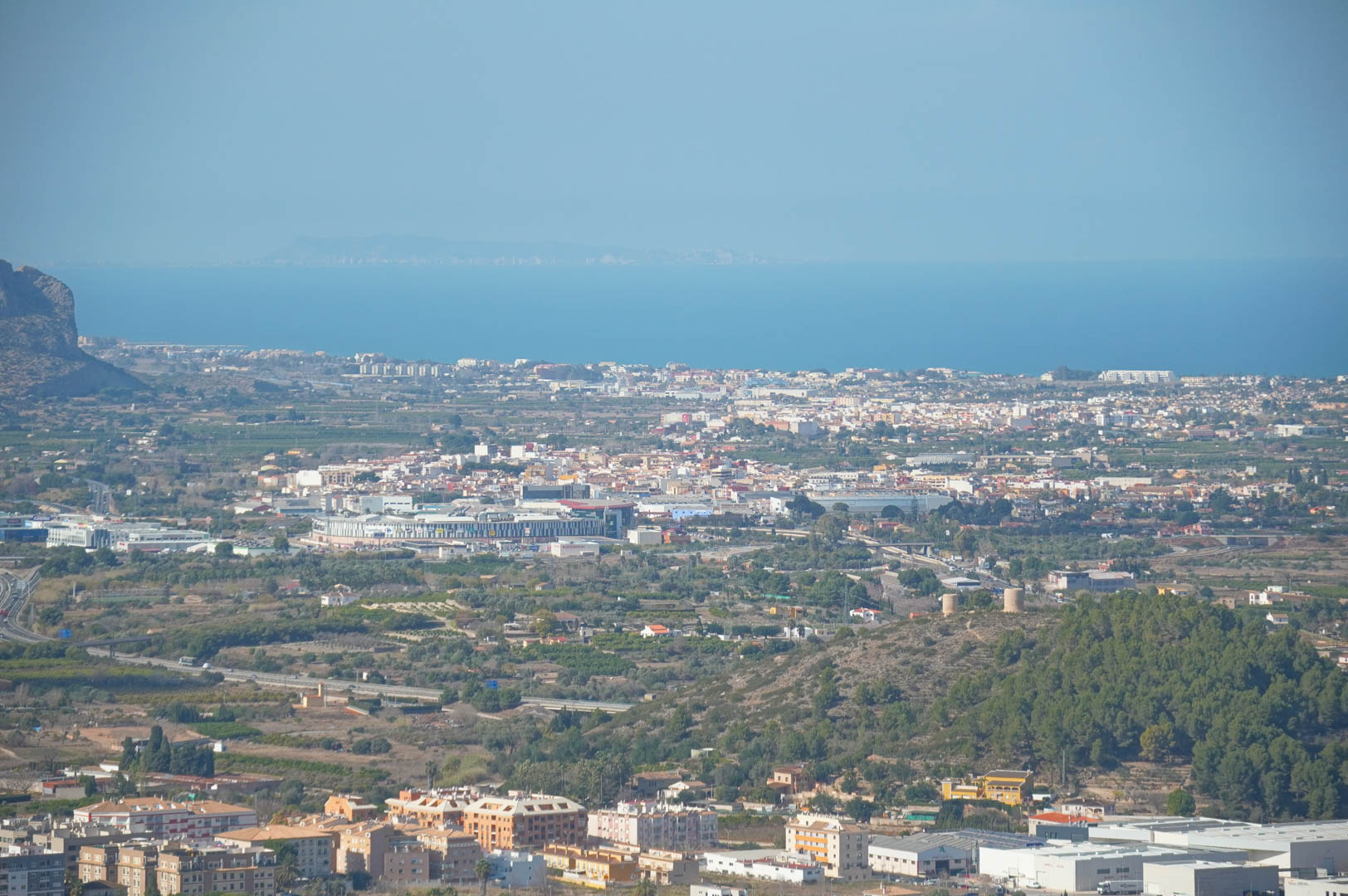Panoramisch uitzicht vanaf het landgoed over de vallei, stedelijke gebieden en de Middellandse Zee aan de horizon onder een heldere hemel.