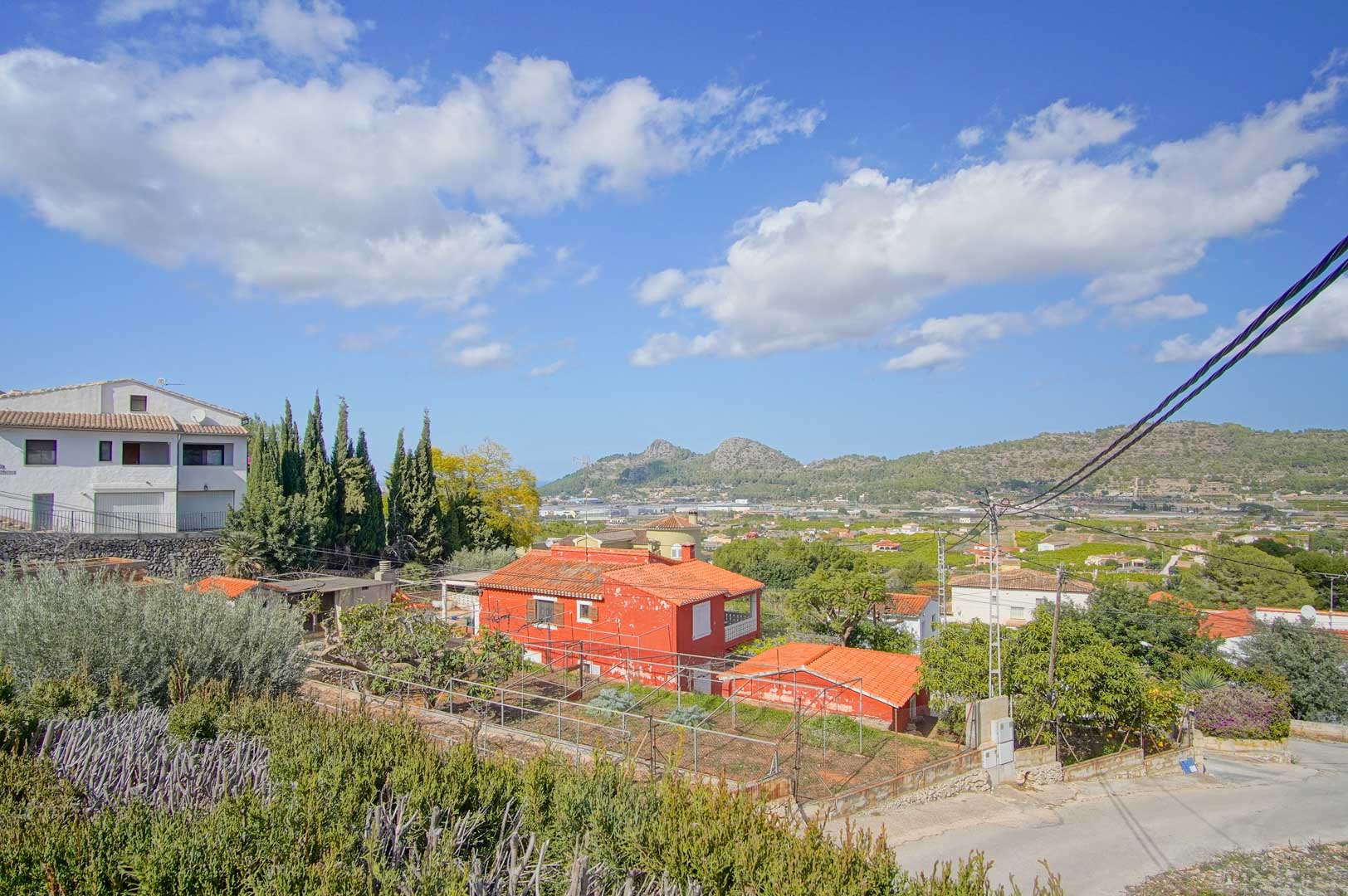 Panoramisch uitzicht vanaf het perceel over de vallei en de bergen van Pedreguer, met mediterrane vegetatie en een rustige woonomgeving onder een heldere hemel.