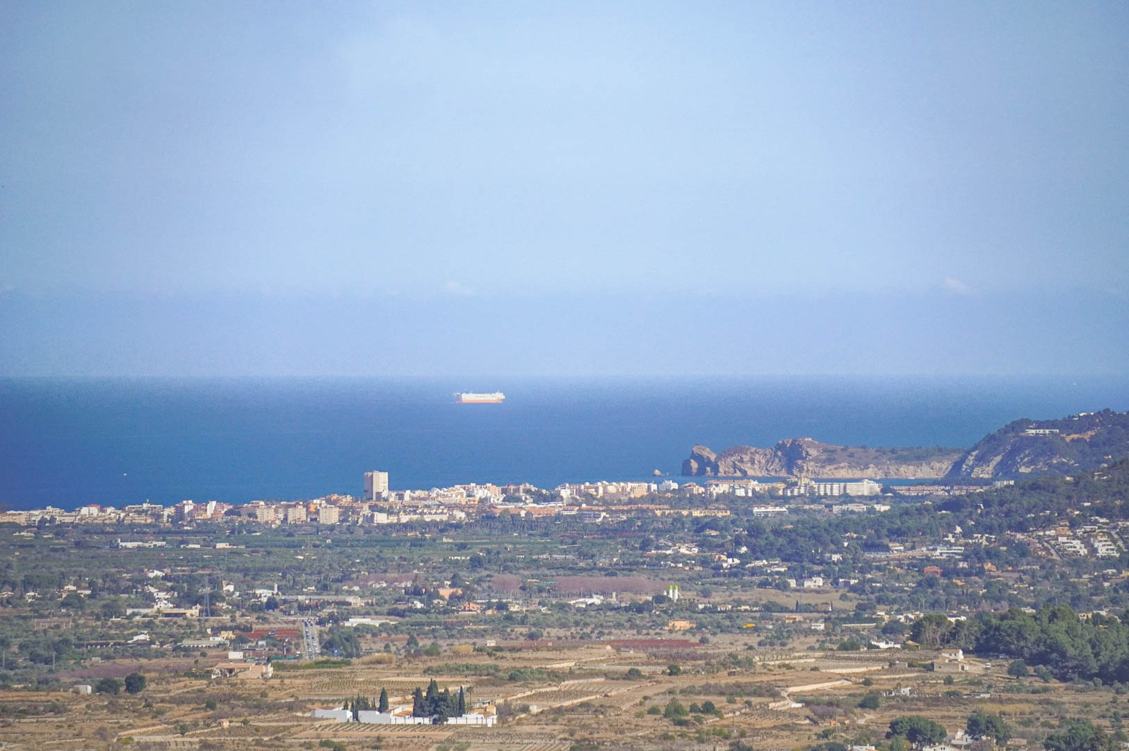 Vrij panoramisch uitzicht op de Middellandse Zeekust, met de skyline van de kuststad en de zee met schepen aan de horizon.