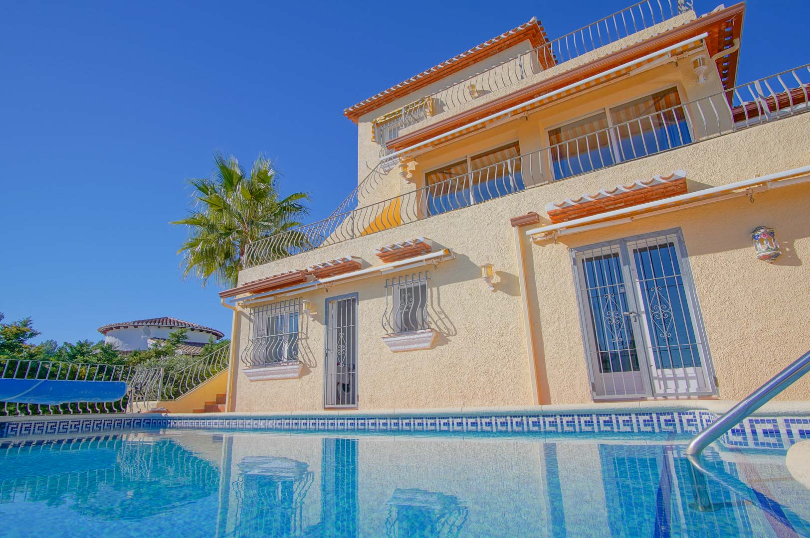 Buitenaanzicht van de villa met drie verdiepingen vanaf het zwembad, met trapsgewijze terrassen, smeedijzeren balustrades en een mediterrane gevel.