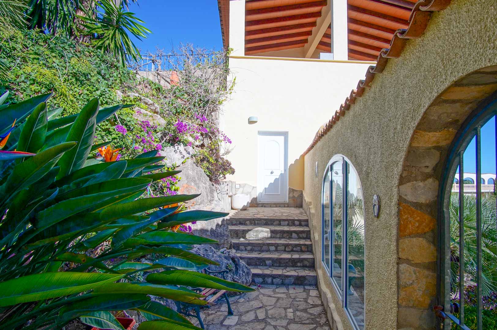 Buitentoegang met natuurstenen trappen, mediterrane beplanting en rustieke stenen muren met boogramen.