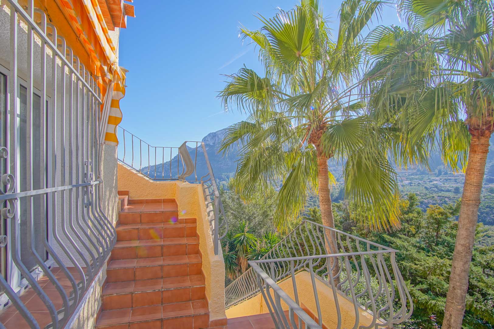 Buitentrap met terracotta tegels en ijzeren balustrades, met uitzicht op de bergen en palmbomen in de mediterrane tuin van de villa.