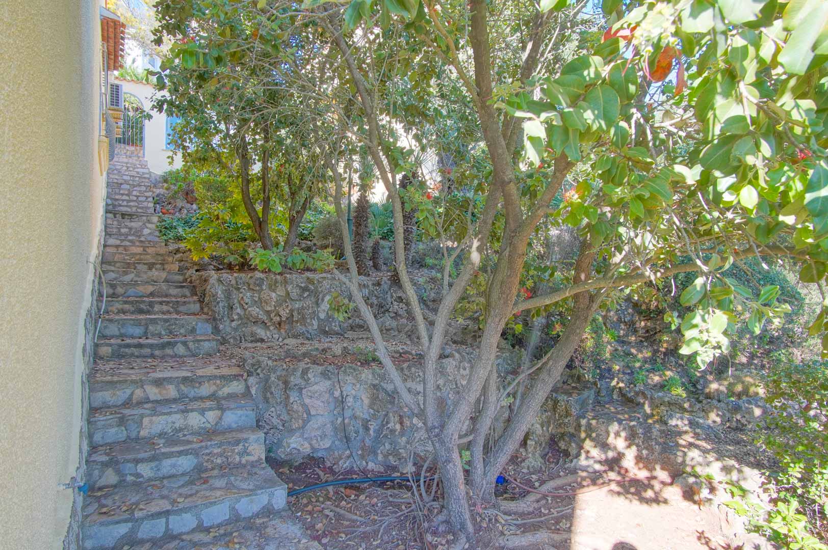 Buitentrap van natuursteen die omhoog leidt door een terrasvormige tuin met stenen muren en volwassen mediterrane beplanting.