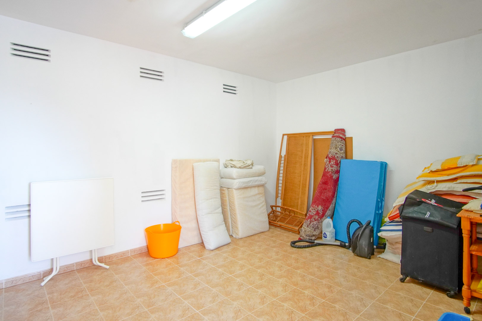 Functionele bergruimte met witte muren, ventilatieroosters en een tegelvloer. Een veelzijdige ruimte met tl-verlichting, geschikt voor diverse opslagdoeleinden.