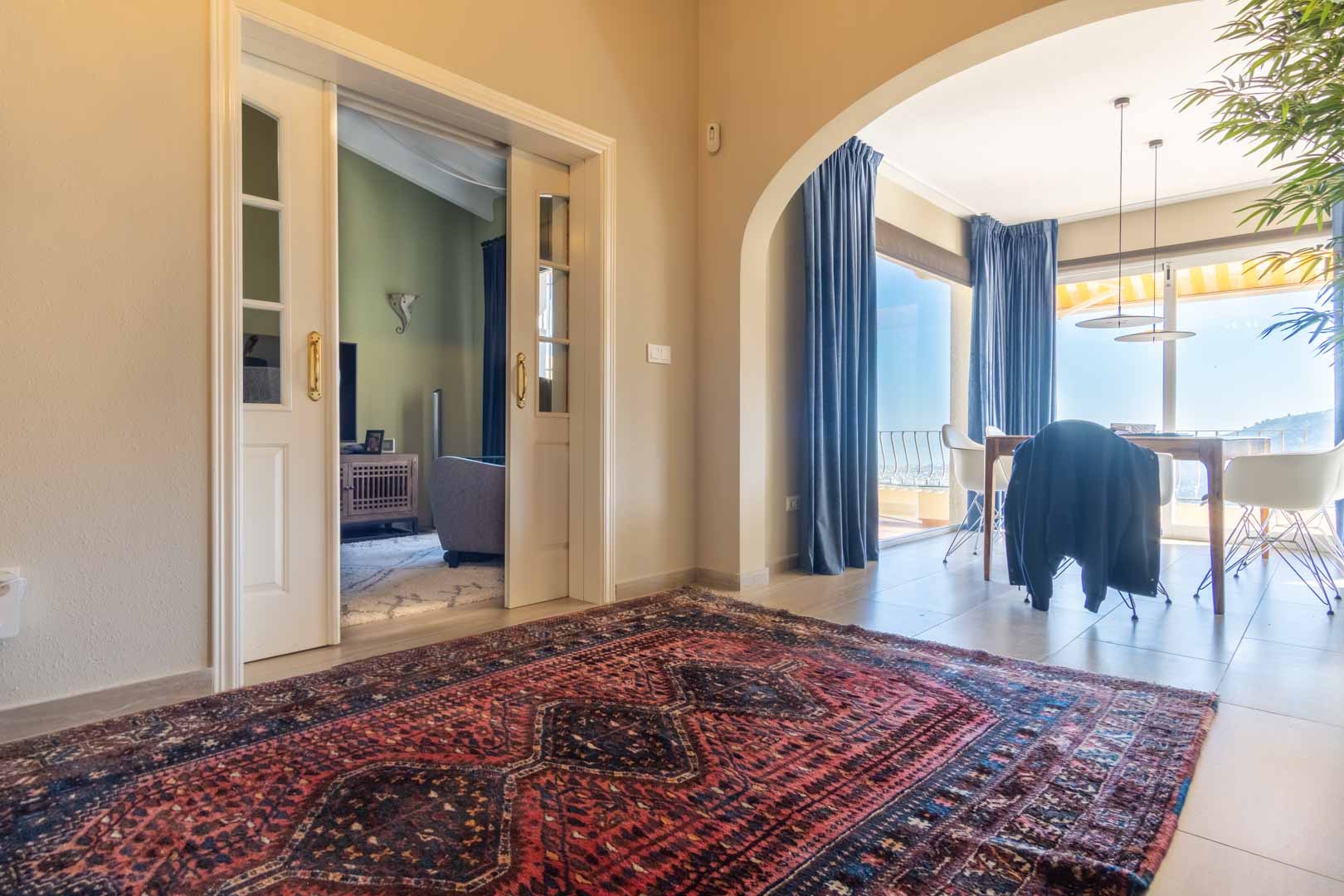 Hal met oosters tapijt, witte glazen schuifdeuren naar de woonkamer en een boog die toegang biedt tot de eetkamer met panoramisch uitzicht op zee.