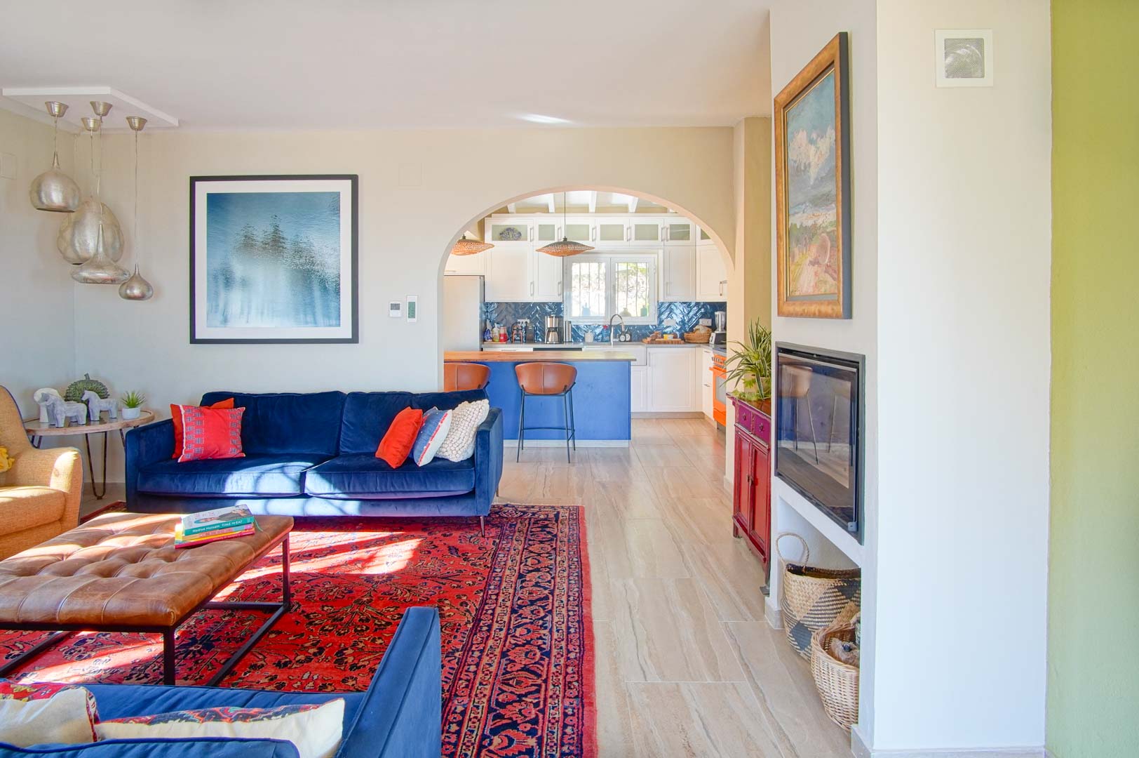 Lichte woonkamer met blauwe fluwelen banken en een ingebouwde haard, verbonden via een toog met een keuken voorzien van een blauw kookeiland.