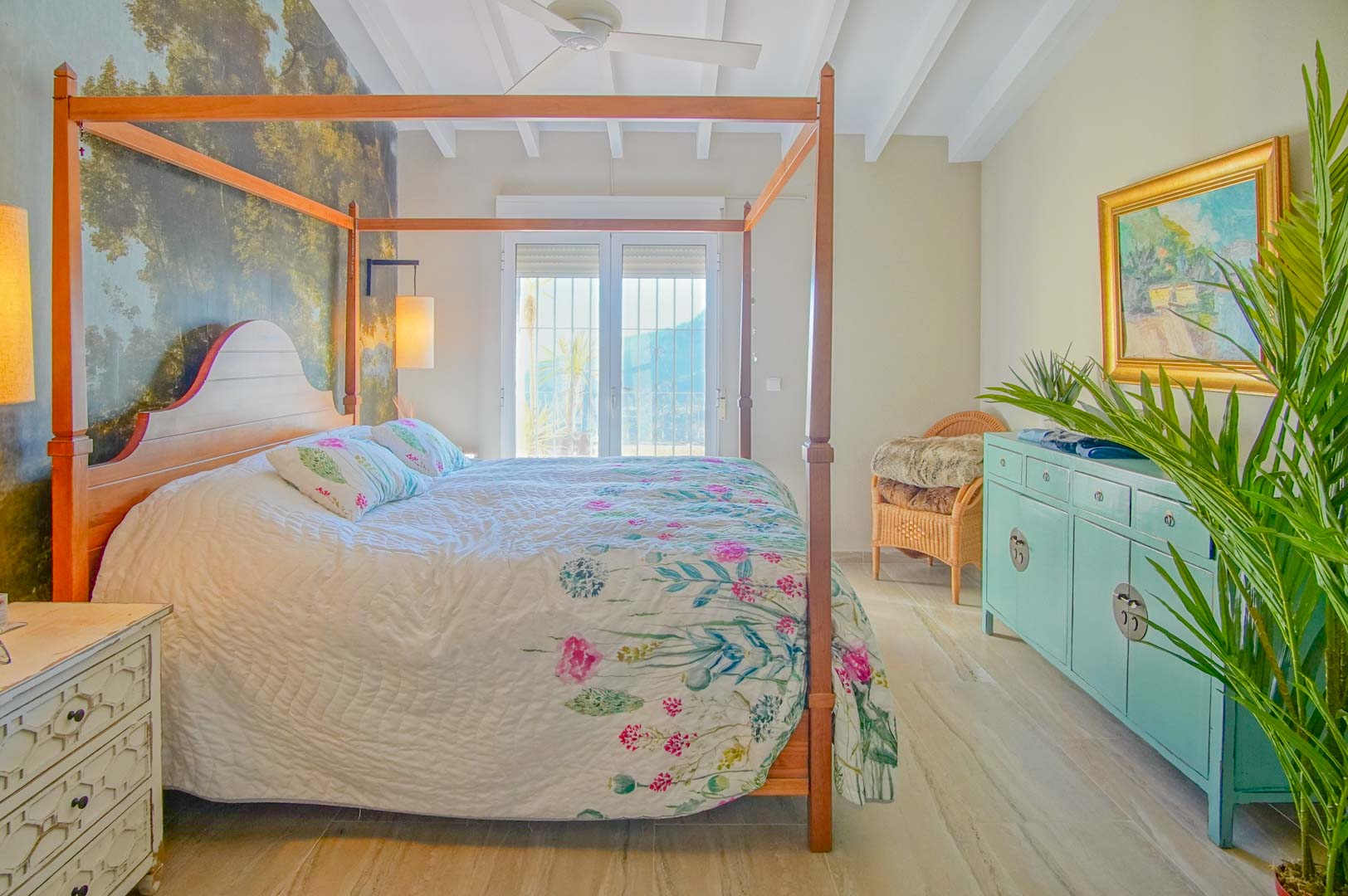 Slaapkamer met houten hemelbed, boswanddecoratie, wit balkenplafond en directe toegang tot het balkon met veel natuurlijk licht.