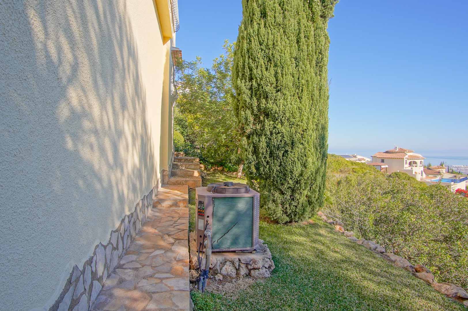 Zijpad van natuursteen langs de gestuukte gevel, met weids uitzicht op zee en een tuin met mediterrane beplanting en een karakteristieke cipres.