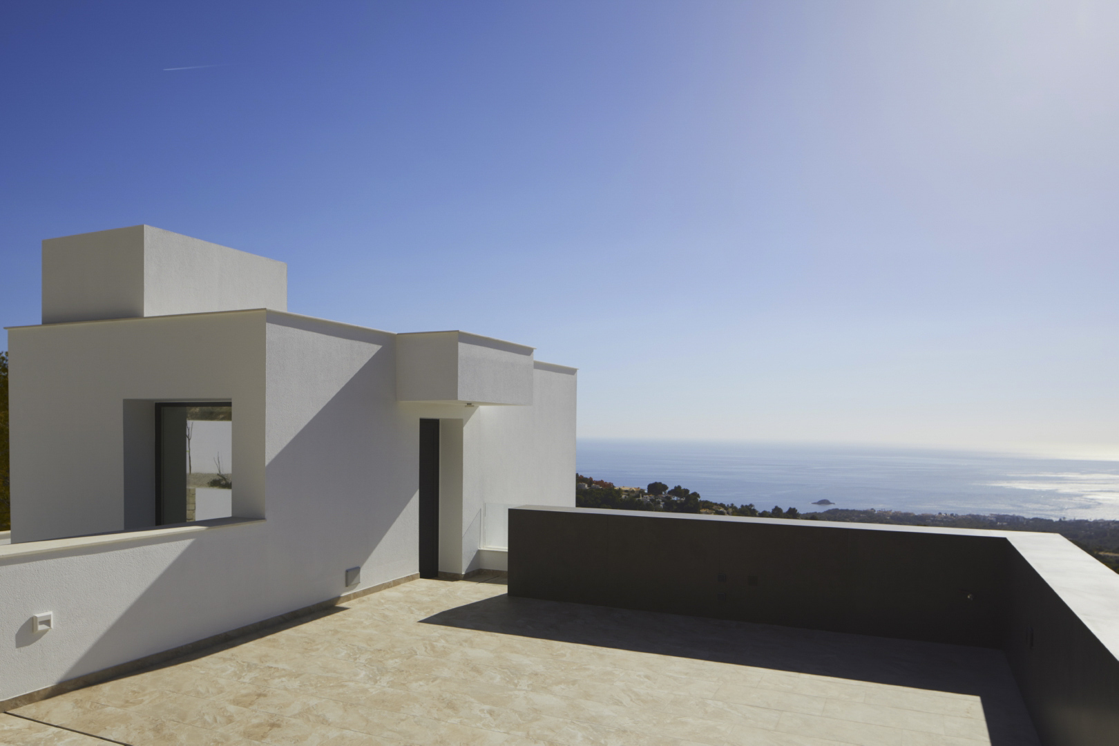 Bovenste terras met minimalistische witte architectuur, keramische tegels en een weids panoramisch uitzicht over de Middellandse Zee.