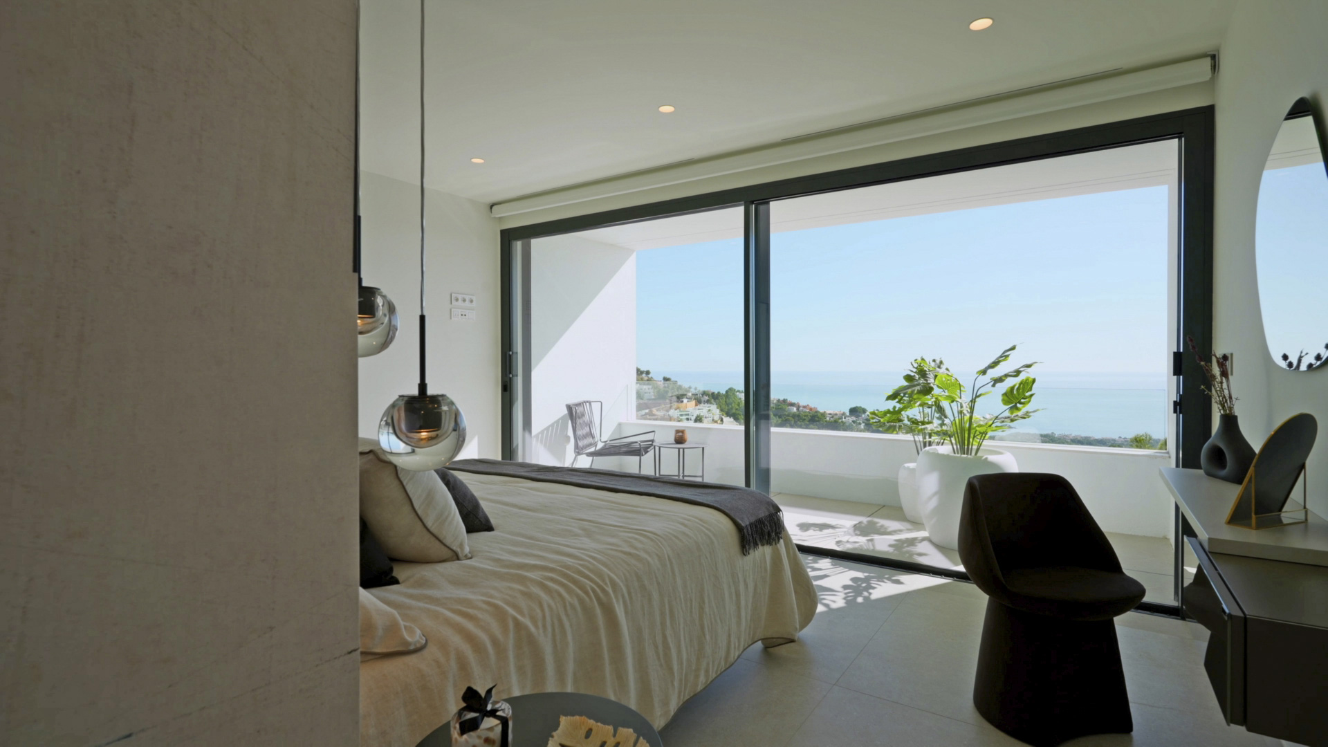 Hoofdslaapkamer met kamerhoge glazen schuifdeuren, privéterras met uitzicht op zee en moderne hanglampen. Voorzien van een minimalistisch bureau.