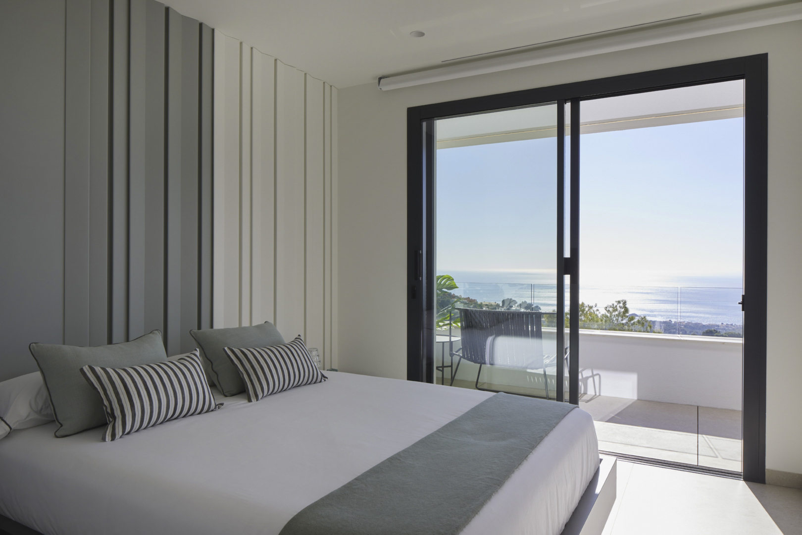 Lichte slaapkamer met decoratieve wandpanelen en directe toegang tot een privéterras met panoramisch uitzicht op de Middellandse Zee.