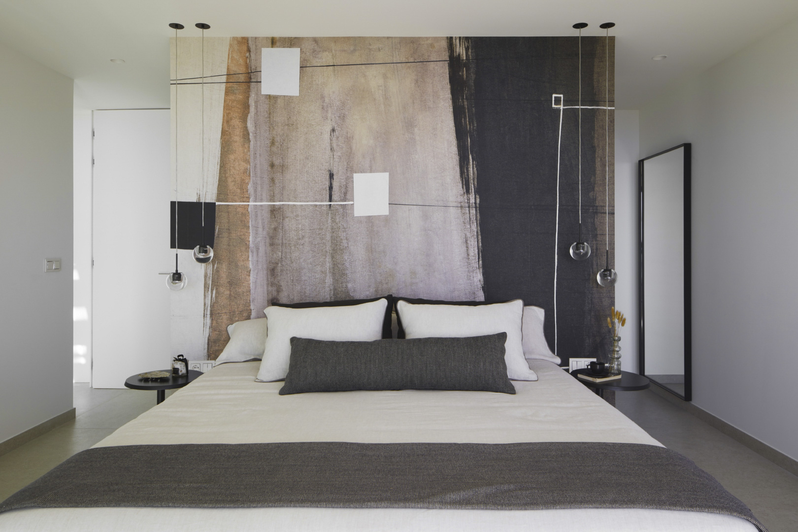 Moderne slaapkamer met een abstracte kunstmuur achter het bed, minimalistische hanglampen en strakke zwarte bijzettafels in een neutraal interieur.