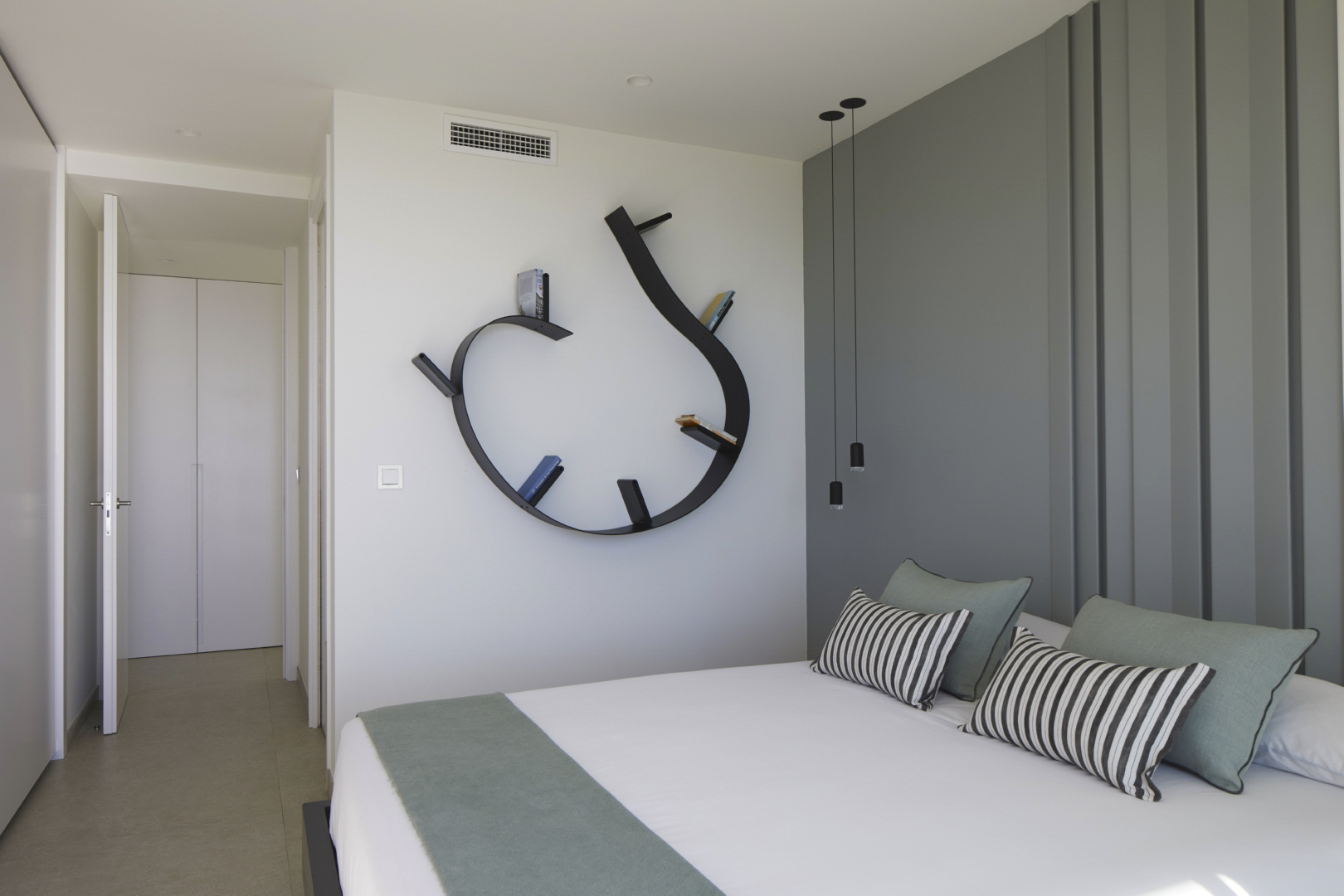 Moderne slaapkamer met een unieke gebogen zwarte wandplank, een grijze accentmuur met panelen en minimalistische hanglampen naast het bed.