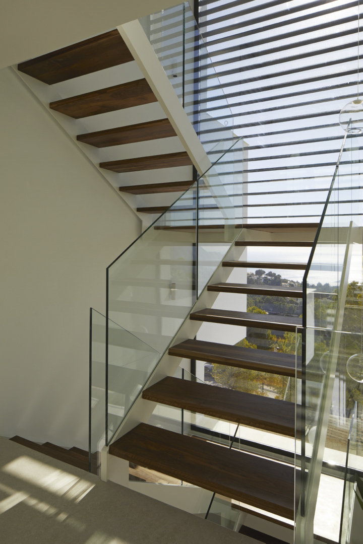 Moderne trap met donkerhouten treden en glazen balustrades, gelegen bij een grote raampartij met panoramisch uitzicht op de Middellandse Zee.