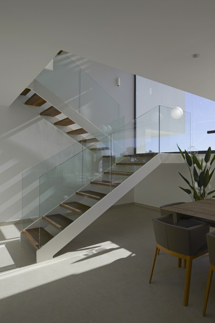 Moderne trap met houten treden en glazen balustrades in een lichte, open ruimte naast de eethoek, verlicht door natuurlijk daglicht.