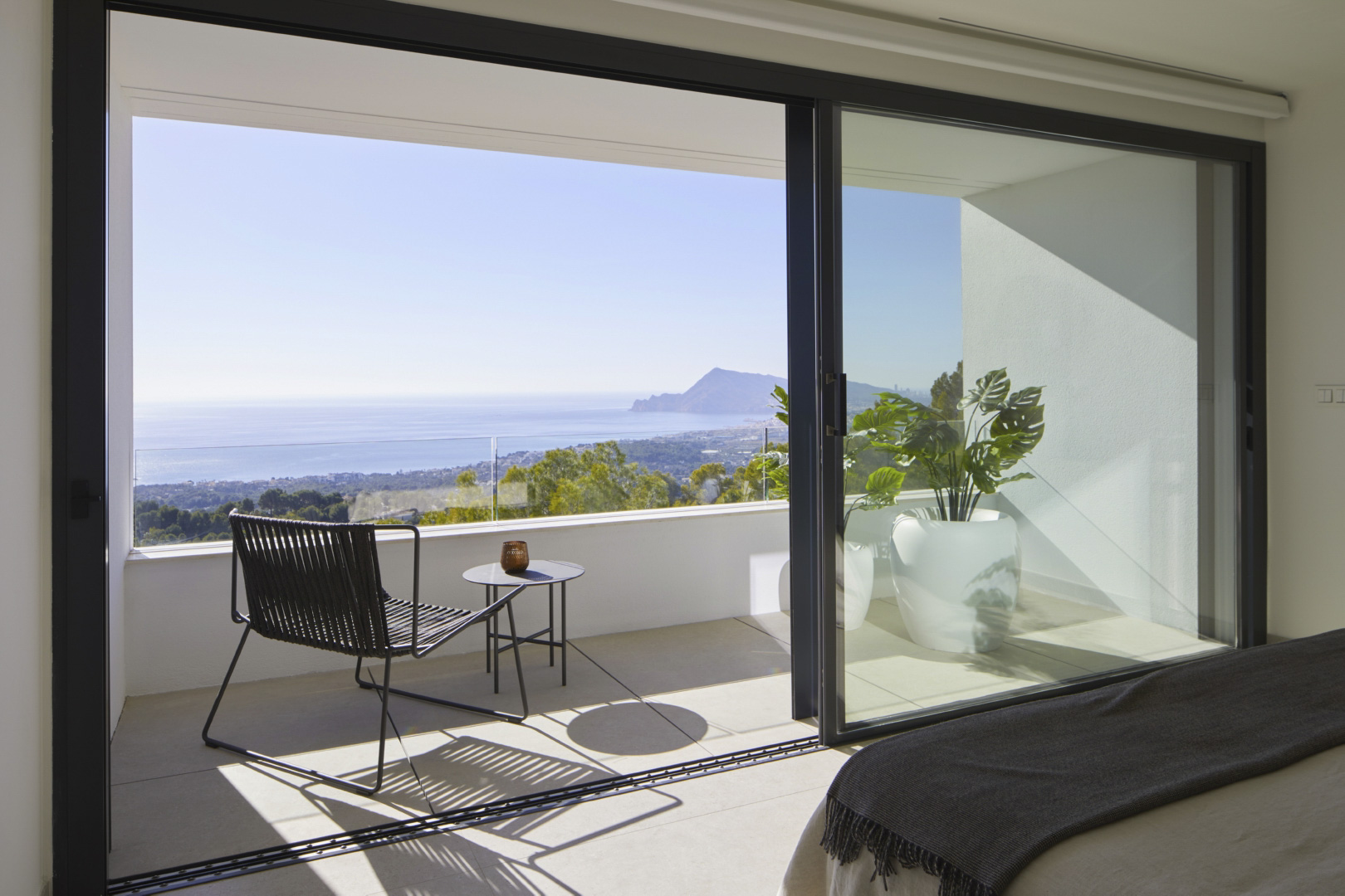 Slaapkamer met grote glazen schuifdeuren naar een privéterras. Voorzien van panoramisch zeezicht, modern buitenmeubilair en een glazen balustrade.