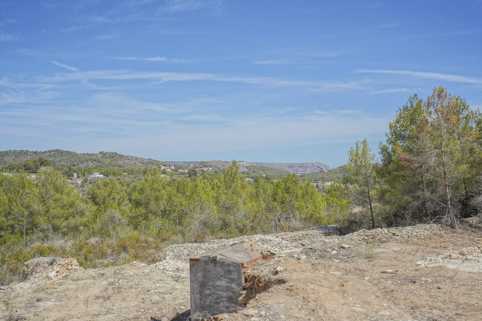 Panoramisch uitzicht vanaf het verhoogde bouwperceel op de mediterrane natuur met pijnbomen en de bergen van Jávea.