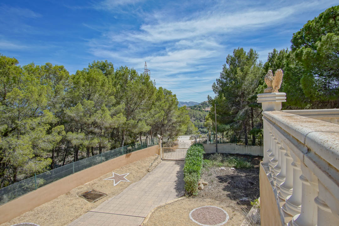 Beveiligde toegang met geplaveide oprit, stenen balustrade met adelaarsbeelden en uitzicht op de omliggende mediterrane dennenbossen.