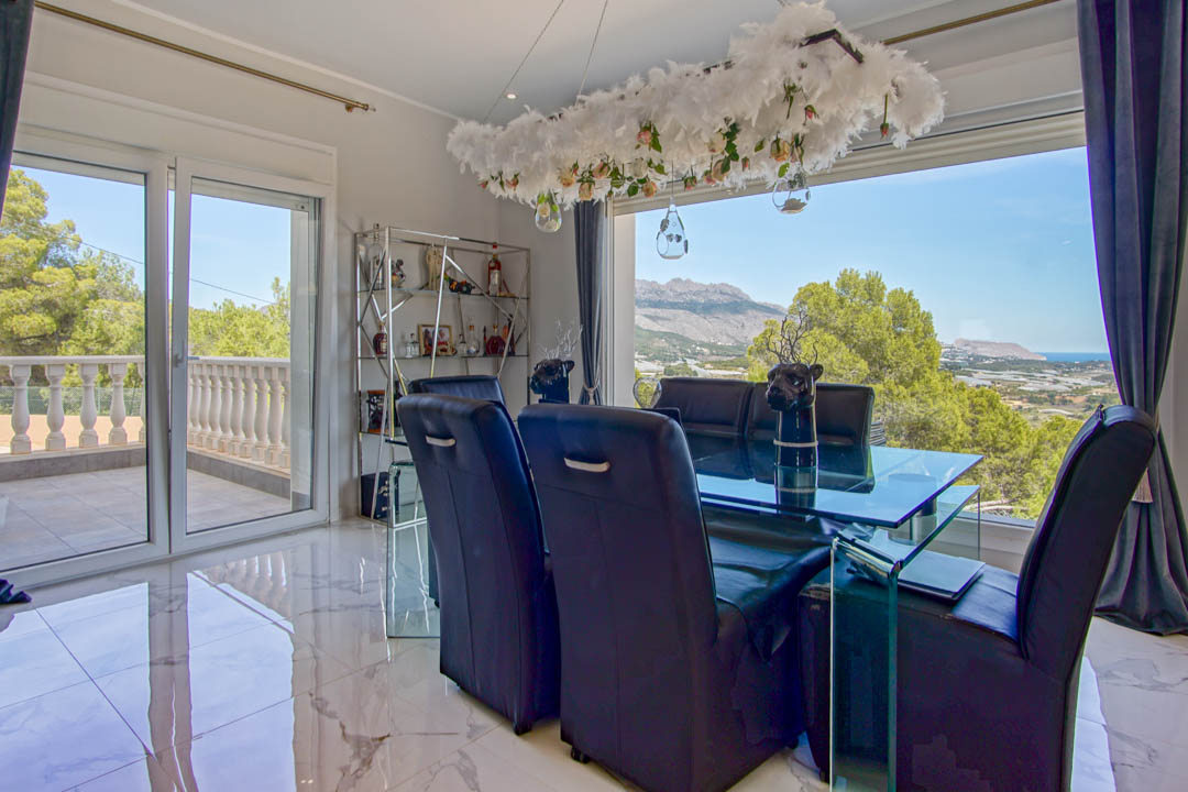 Formele eetkamer met marmeren vloer, glazen tafel en zwarte lederen stoelen, met een weids panoramisch uitzicht op de bergen en de zee via grote raampartijen.