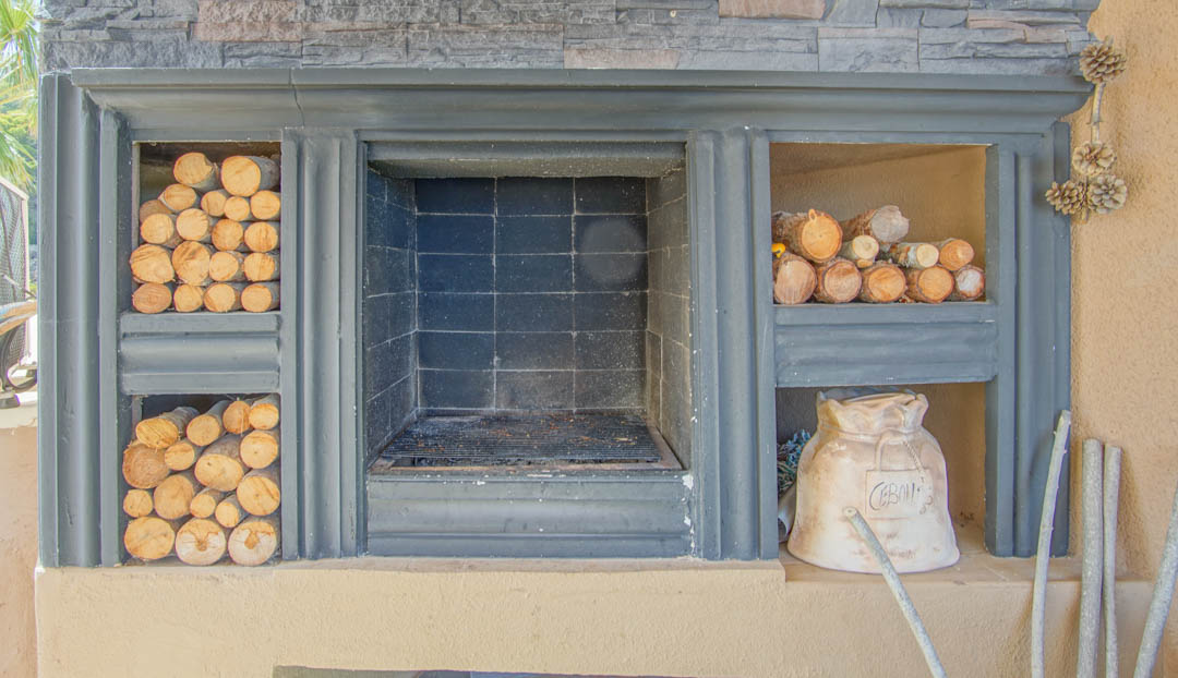 Ingebouwde buitenhaard met centrale barbecue, natuurstenen afwerking en zijvakken voor de opslag van haardhout.