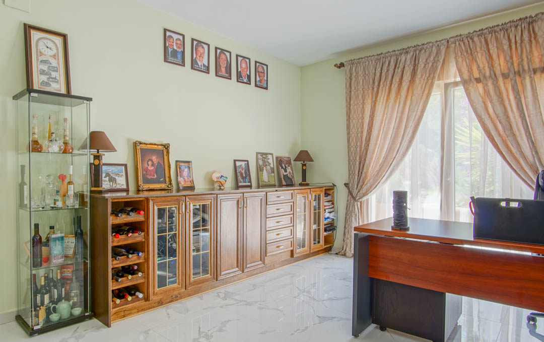 Licht kantoor met marmeren vloer, houten bureau en een dressoir met geïntegreerd wijnrek en glazen vitrinekasten.