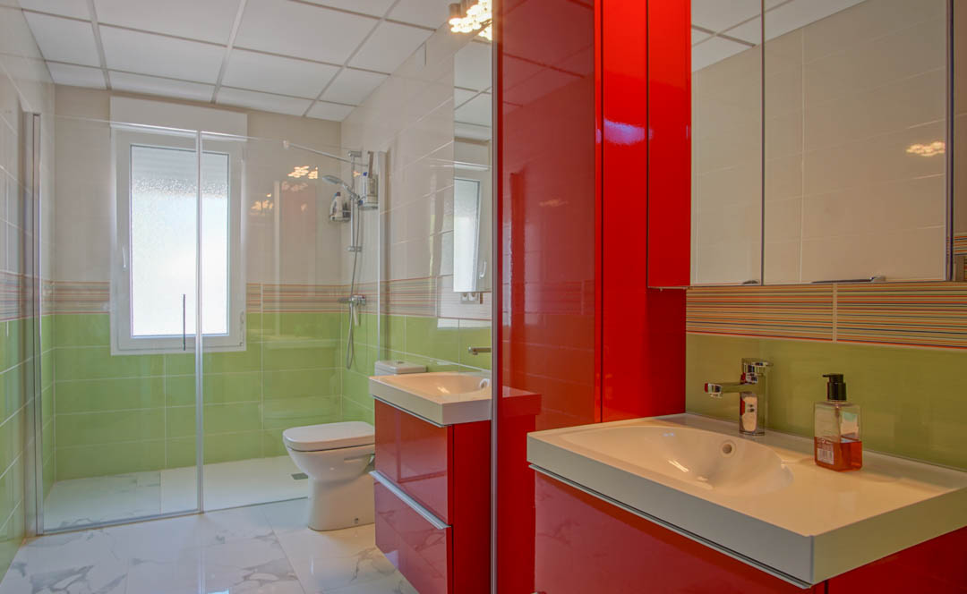 Moderne badkamer met hoogglans rood meubilair, een glazen inloopdouche en wandtegels in frisse groentinten gecombineerd met marmerlook vloeren.