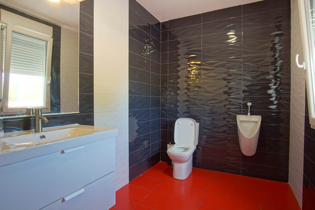 Moderne badkamer met rode vloertegels, donkere wandtegels met golfreliëf, een wit wastafelmeubel en een wandgemonteerd urinoir.