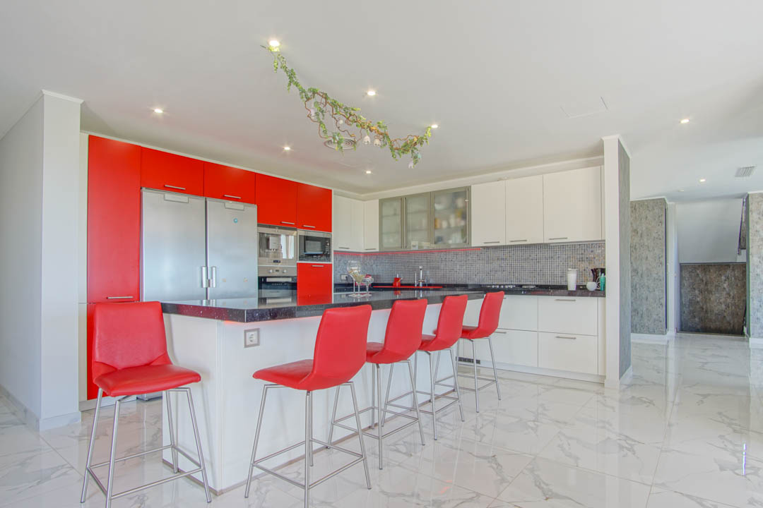 Moderne keuken met een zwart granieten eiland, rode barkrukken en hoogglanskasten. Voorzien van een witte marmeren vloer en geïntegreerde roestvrijstalen apparatuur.
