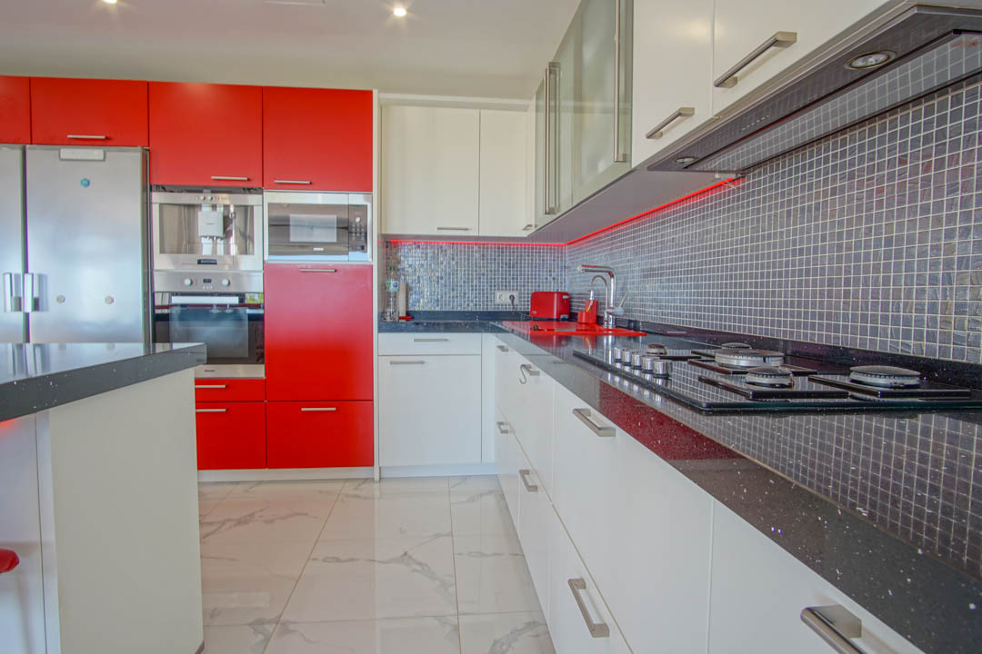 Moderne keuken met hoogglans rode en witte kasten, zwart granieten werkbladen en een grijze mozaïek achterwand met geïntegreerde led-verlichting.