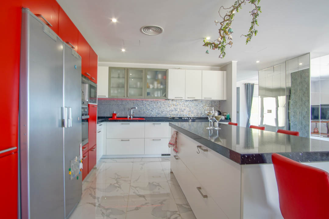 Moderne keuken met rood-witte kastfronten, een royaal kookeiland met donker blad en een gepolijste vloer met een luxe marmeruitstraling.
