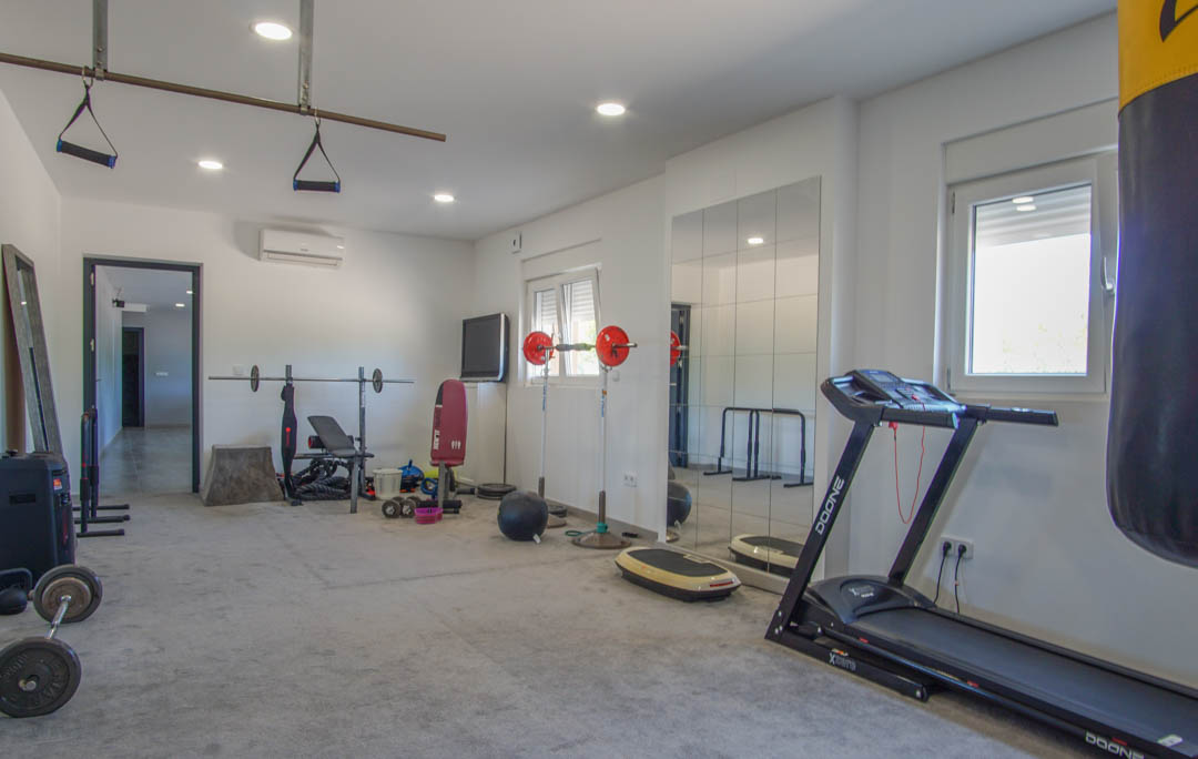 Privé fitnessruimte voorzien van een loopband, bokszak en gewichten. De ruimte beschikt over wandspiegels, inbouwspots en airconditioning.