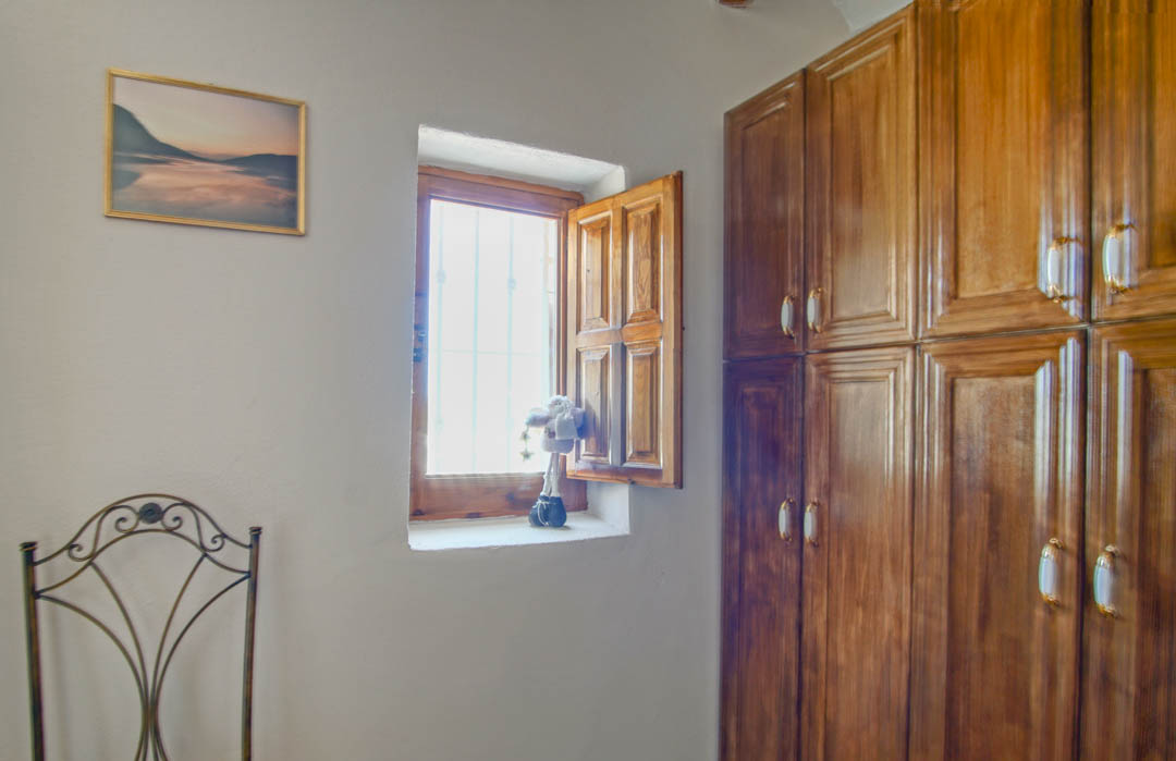 Rustieke kamer met een inbouwkast van massief hout, een traditioneel raam met houten luiken en een decoratieve smeedijzeren stoel.
