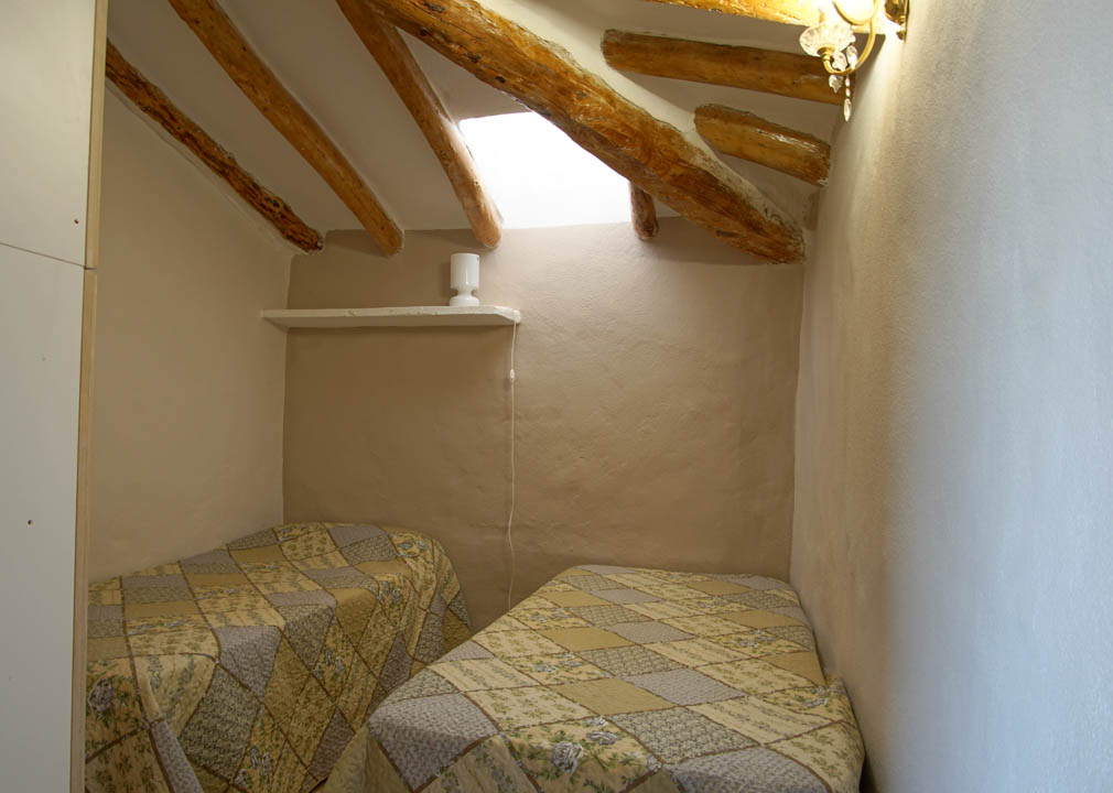Rustieke slaapkamer met schuine plafonds, authentieke houten balken en een dakraam. De kamer is voorzien van twee eenpersoonsbedden en muren met natuurlijk pleisterwerk.