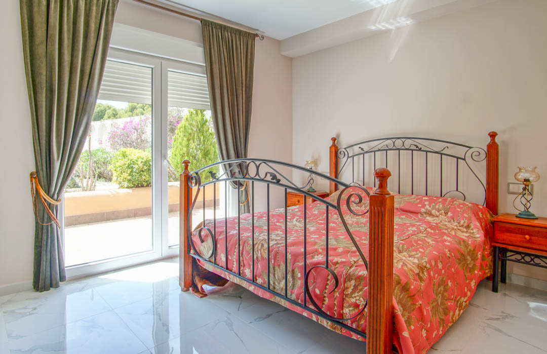 Slaapkamer met gepolijste marmeren vloer, een bedframe van smeedijzer en hout, en directe toegang tot het terras via grote glazen deuren.