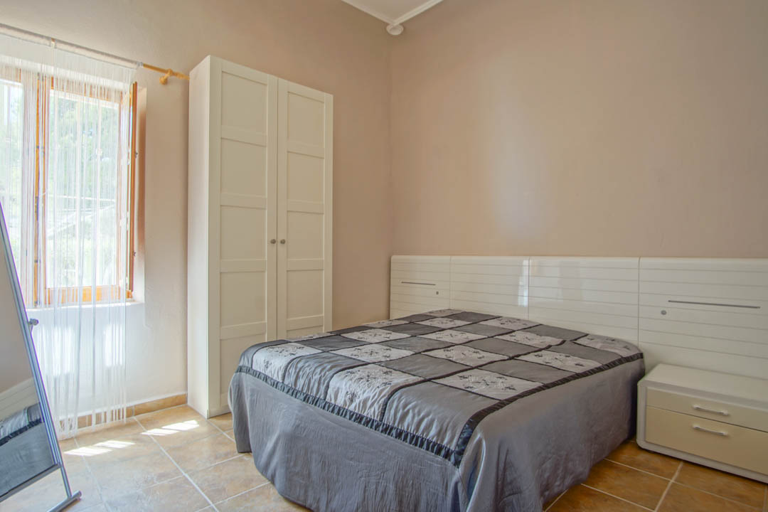 Slaapkamer met keramische tegelvloer, een vrijstaande witte kledingkast en een modern hoofdbord met geïntegreerde nachtkastjes.