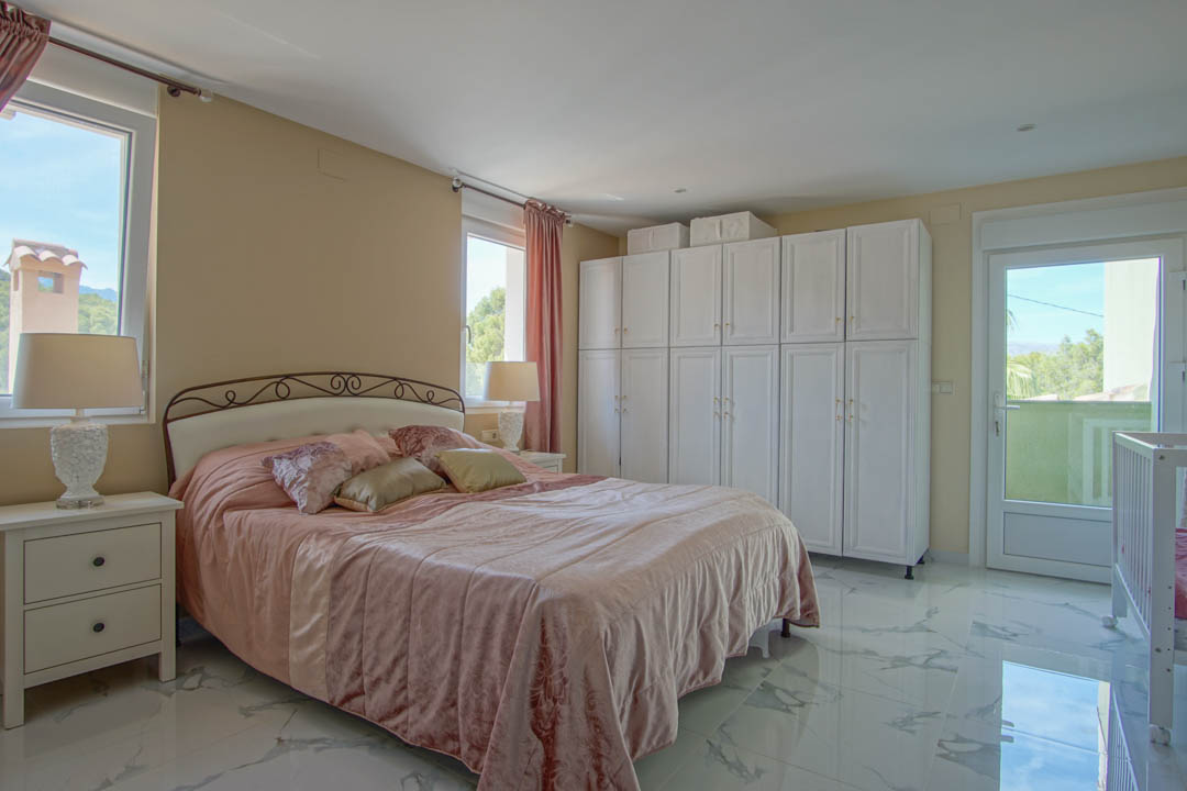 Slaapkamer met porseleinen vloer met marmerlook, ruime witte kastenwand en toegang tot een balkon met vrij uitzicht op de bergen.