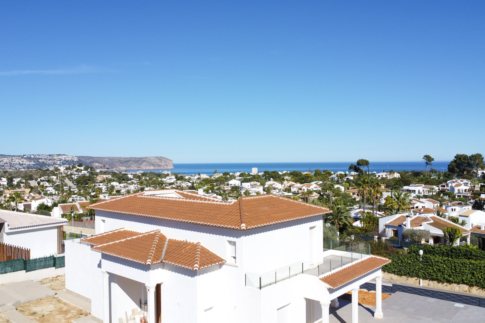 Exterieurzicht van de villa met witte gevels en pannendaken, voorzien van terrassen met glazen balustrades en panoramisch uitzicht over de Middellandse Zee.