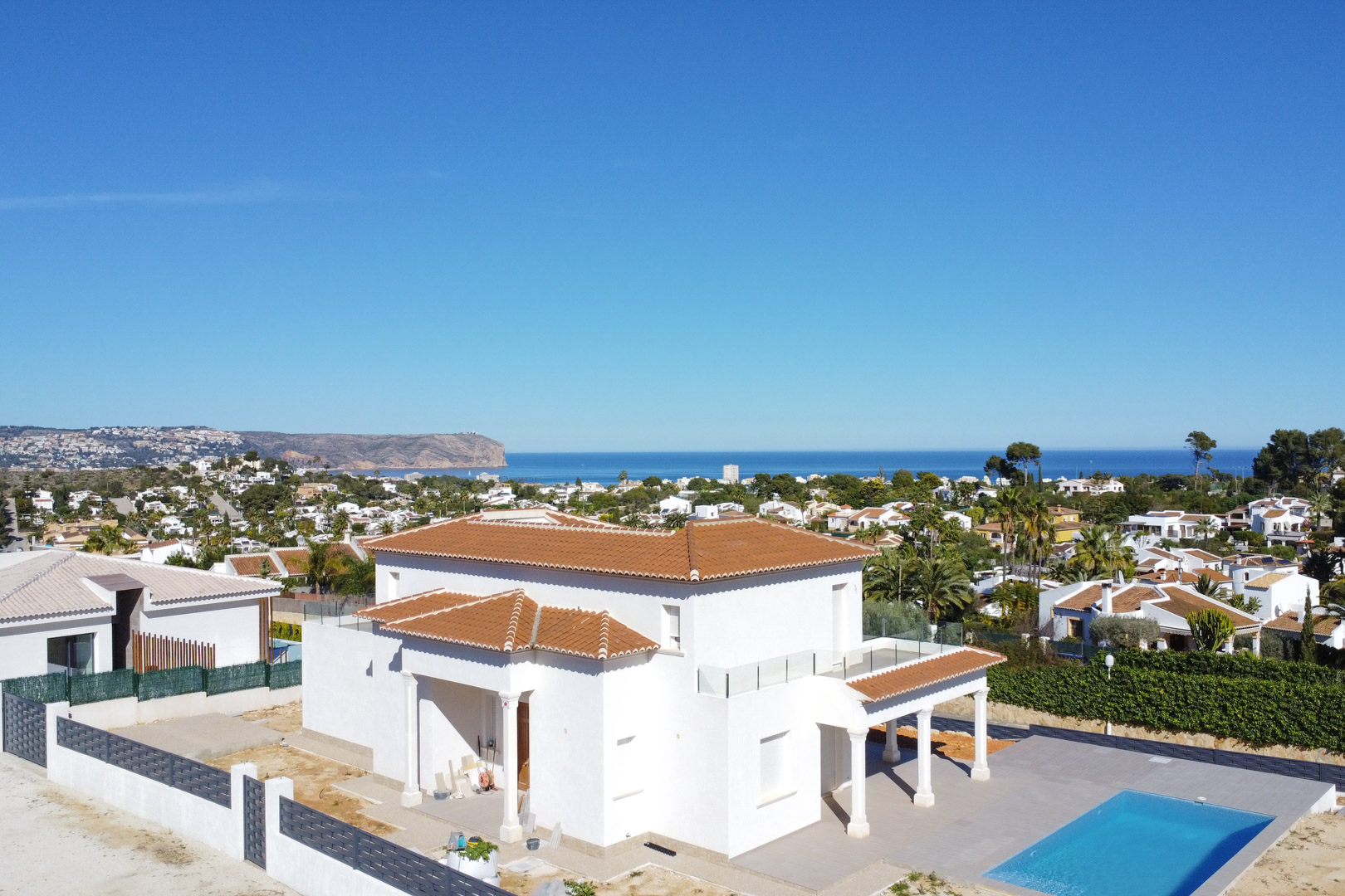 Luchtfoto van de witte villa met pannendak, rechthoekig zwembad en terrassen met glazen balustrades die een weids uitzicht bieden over de Middellandse Zee.