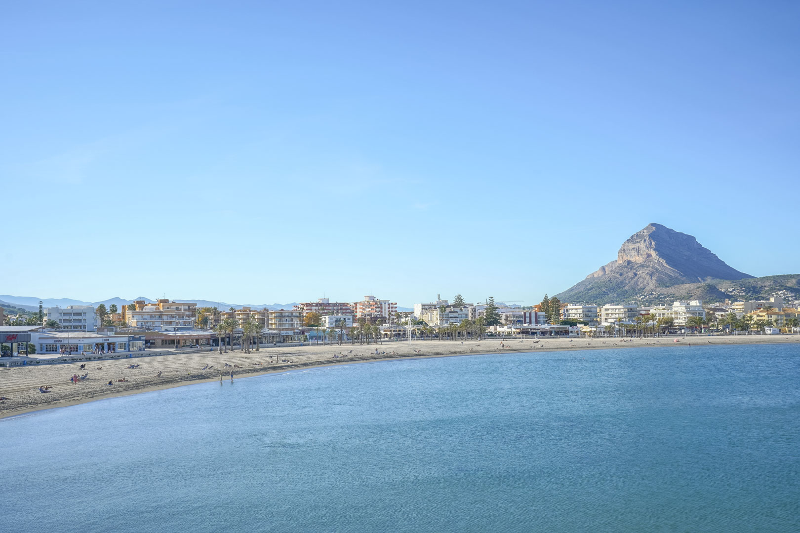 Panoramisch uitzicht op het Arenal-strand in Jávea, met de zandkust, het heldere water en de karakteristieke Montgó-berg op de achtergrond.