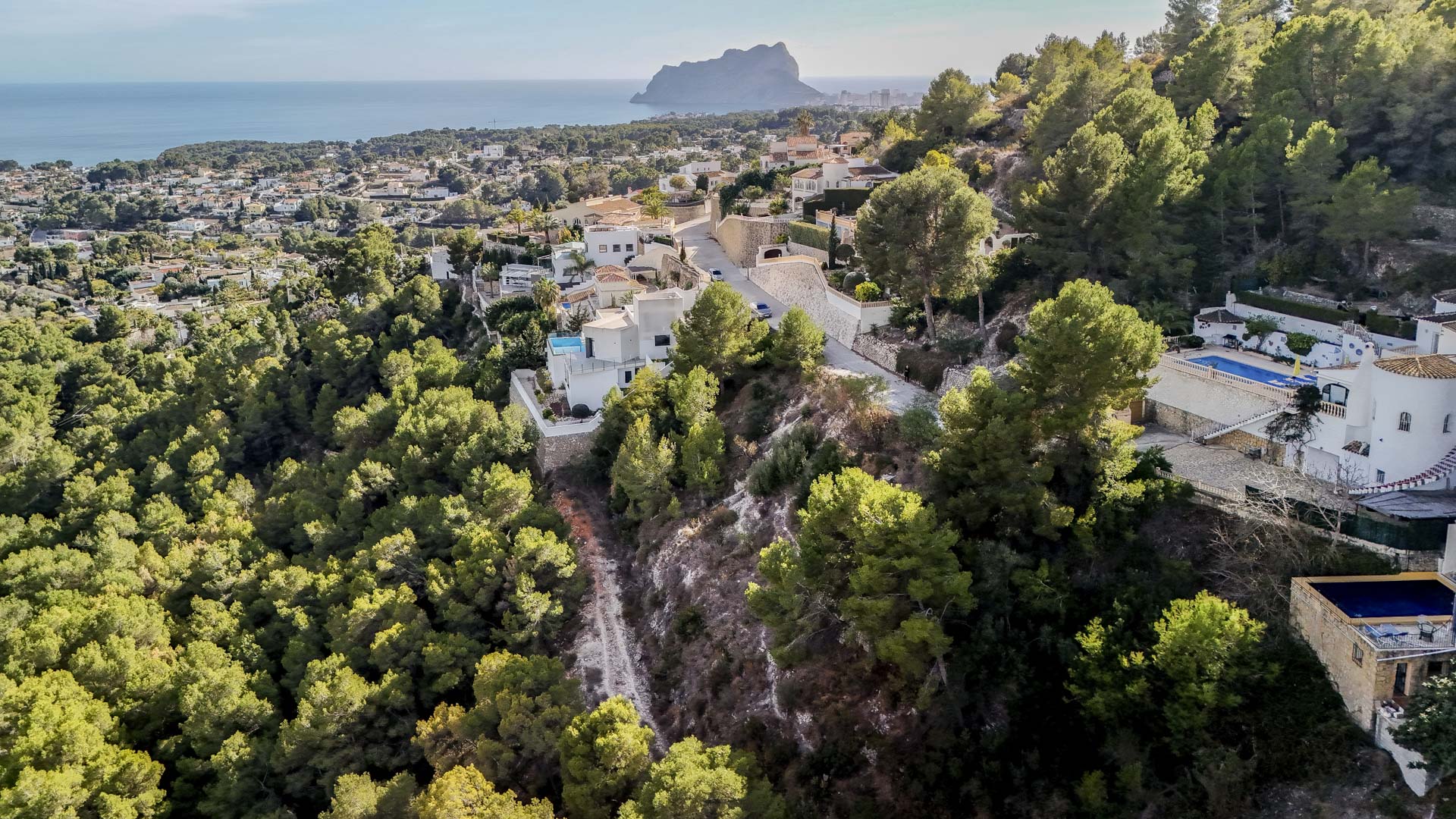 Luchtfoto van de woonwijk in Benissa, met uitzicht op de Peñón de Ifach en de uitgestrekte beschermde groene zone rondom de percelen.