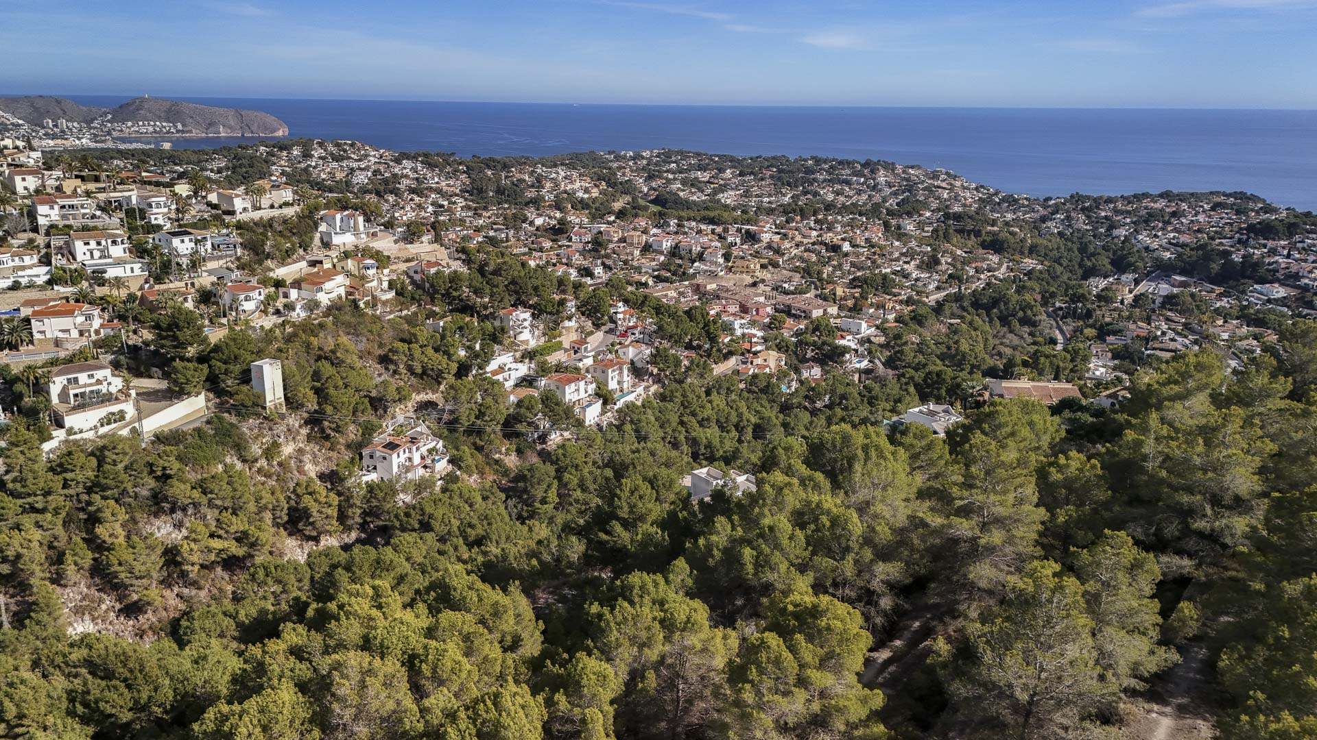 Luchtfoto van de woonwijk in Benissa, omgeven door dichte dennenbossen met een weids panoramisch uitzicht over de Middellandse Zee.