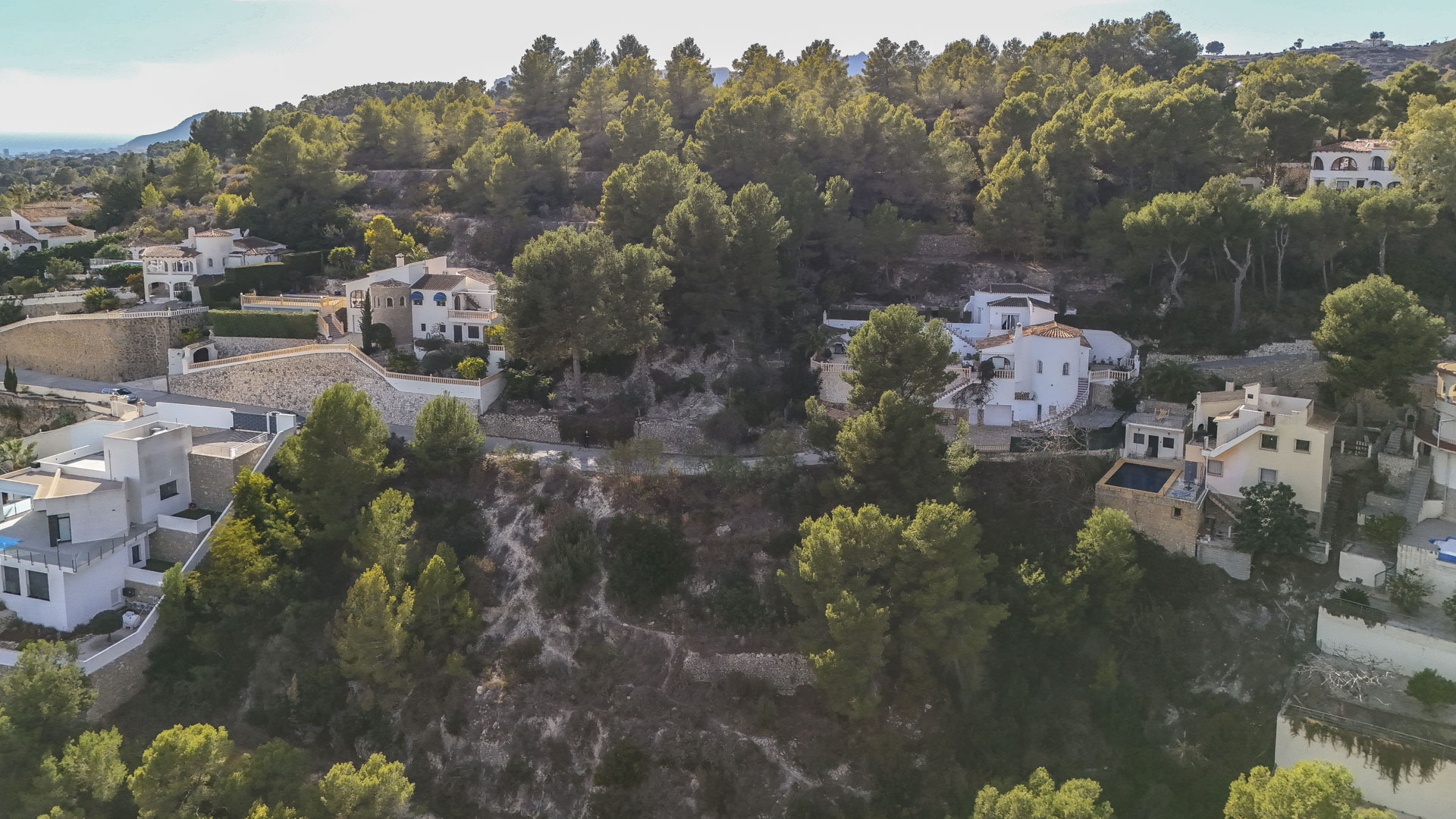 Luchtfoto van residentiële percelen in Benissa, omgeven door een dicht dennenbos met natuurstenen muren en uitzicht op de Middellandse Zee in de verte.