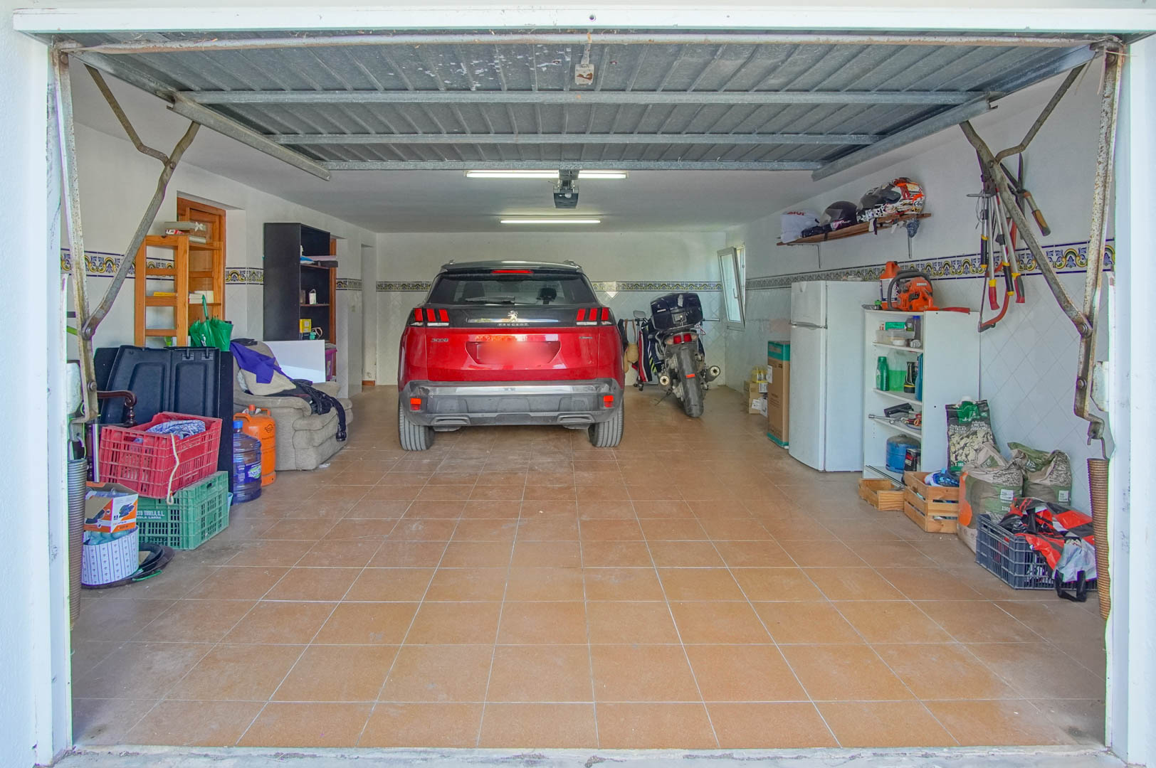 Afgesloten garage in het souterrain met keramische tegelvloer, tl-verlichting en multifunctionele ruimte voor voertuigen en opslag.