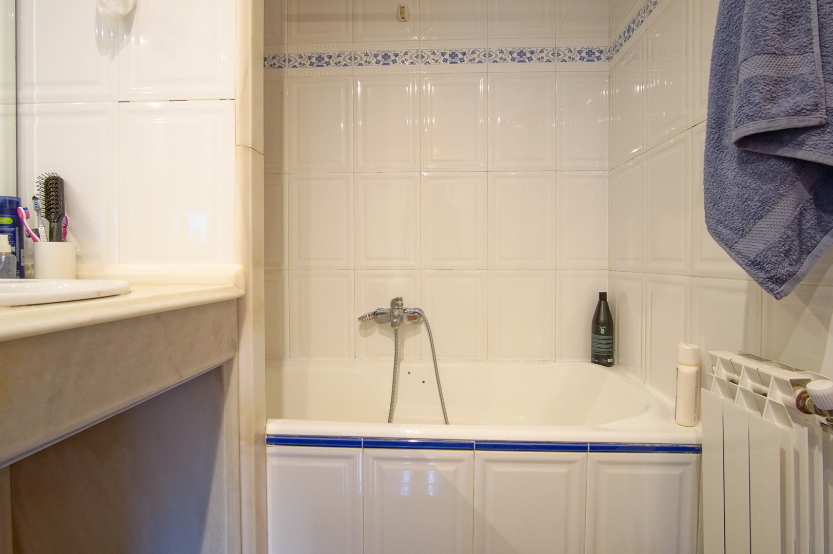 Badkamer met ligbad, witte wandtegels met blauwe bloemendetails en een marmeren wastafelblad. Voorzien van een radiator en klassieke chromen kranen.